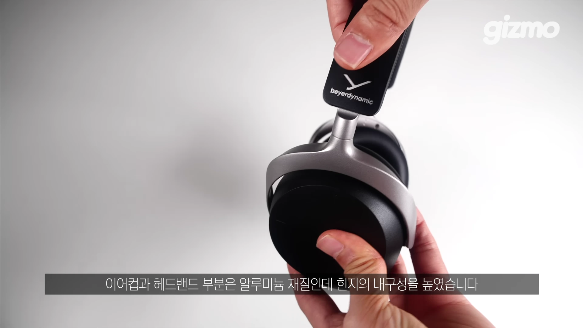 두 손으로 검은색 무선 헤드폰의 이어컵과 헤드밴드 연결 부위를 잡고 힌지의 움직임을 보여주는 모습