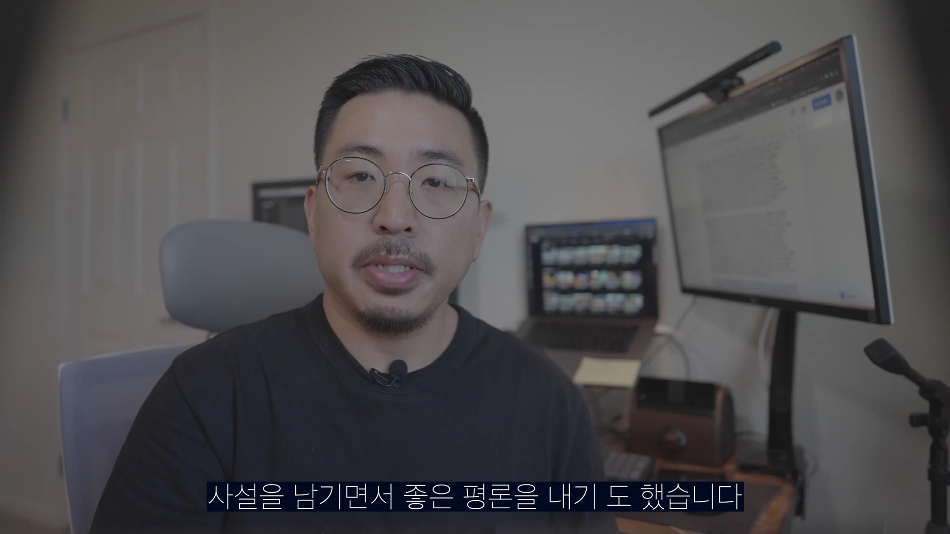 안경을 쓴 남성이 실내 책상 앞에 앉아 카메라를 응시하며 이야기하고 있습니다. 배경에는 컴퓨터 모니터와 작업 장비가 보입니다.