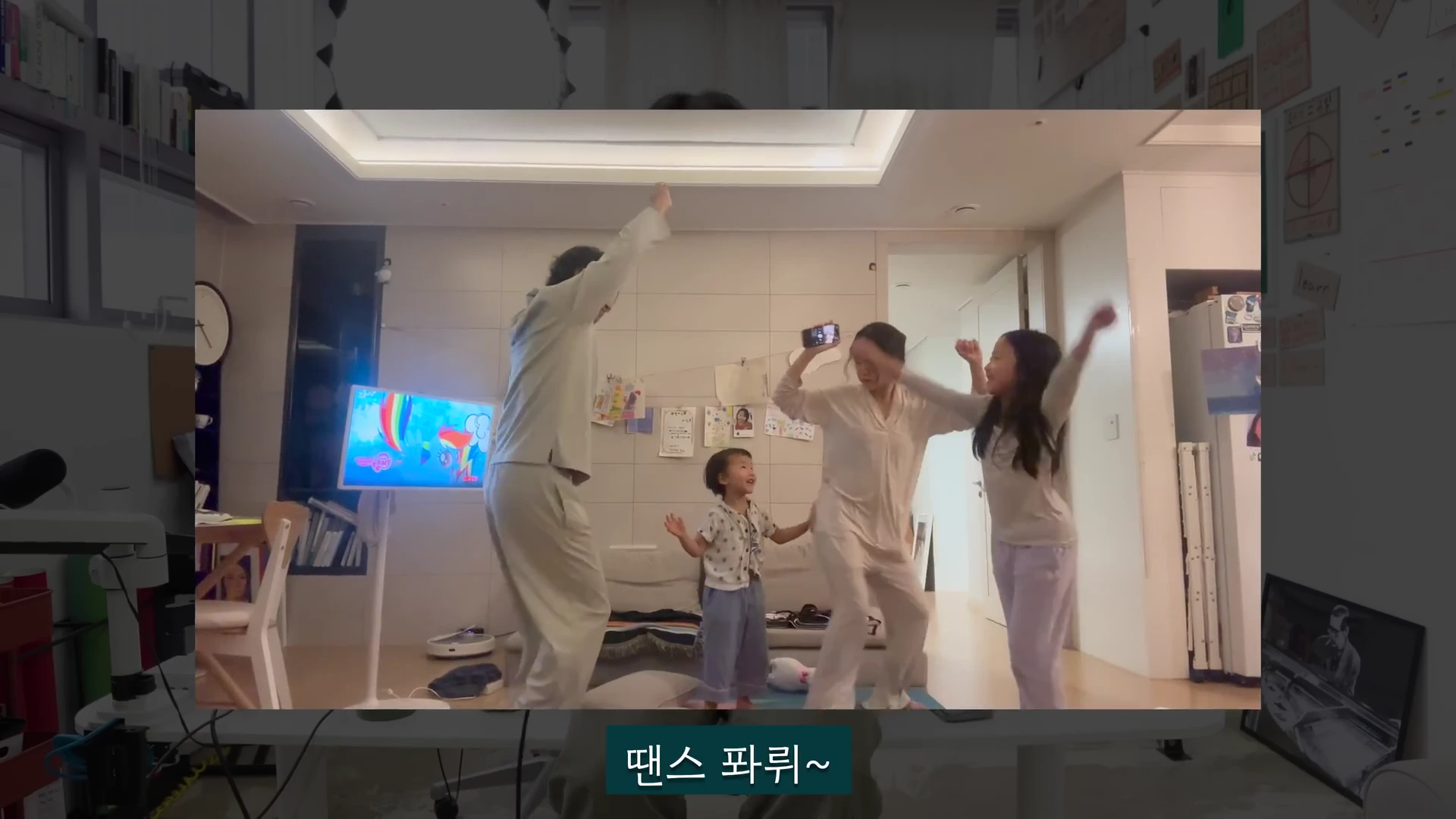 실내 거실에서 부모와 두 자녀가 편안한 잠옷 차림으로 신나게 춤을 추고 있는 모습