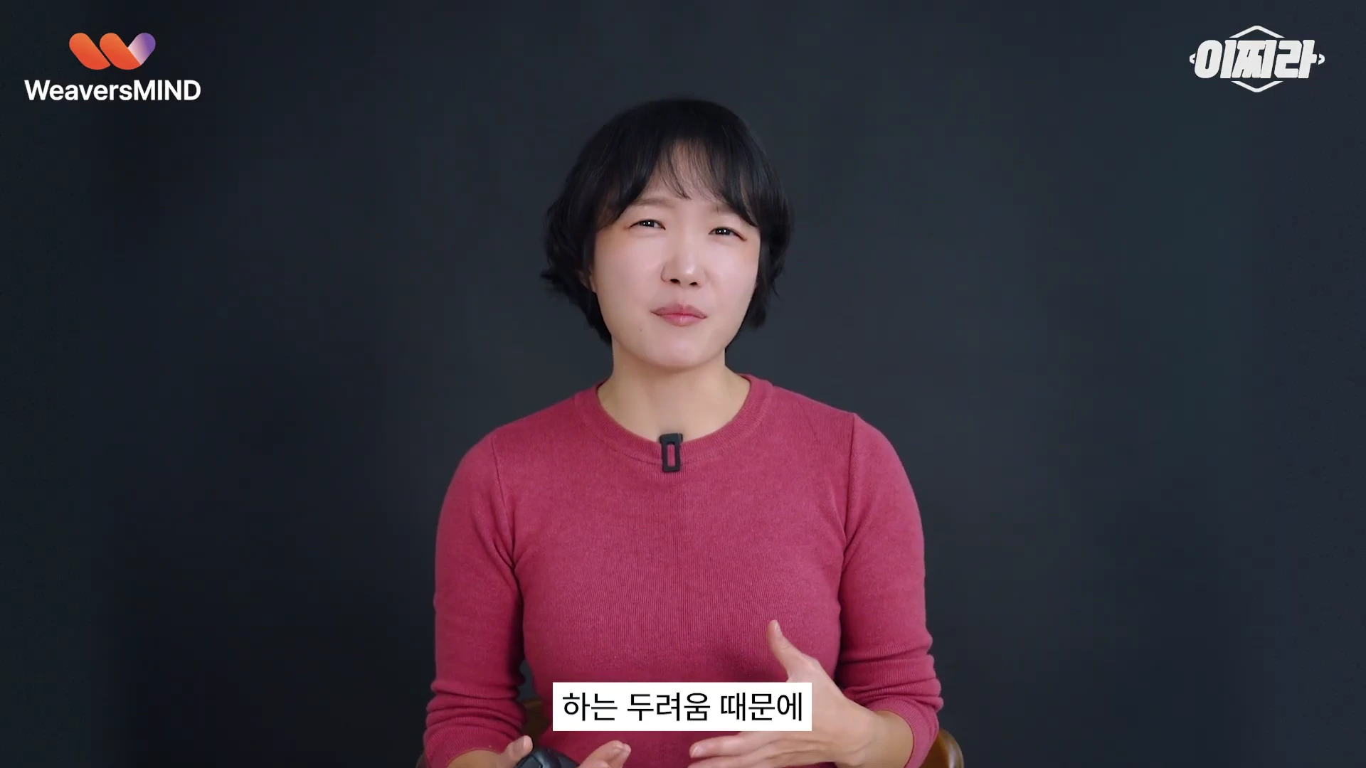 단발머리의 여성 출연자가 어두운 배경 앞에서 무언가를 설명하며 제스처를 취하고 있는 영상 화면입니다.