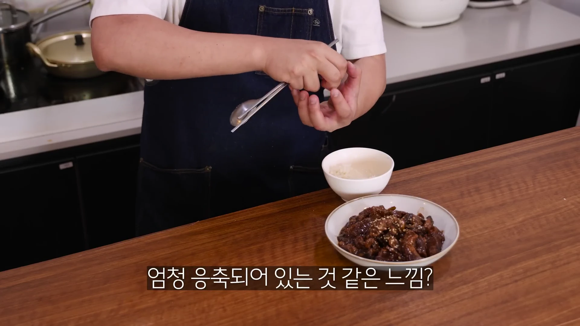 요리사가 앞치마를 입고 조리대 앞에서 요리한 갈비찜이 담긴 접시를 보여주고 있는 모습.