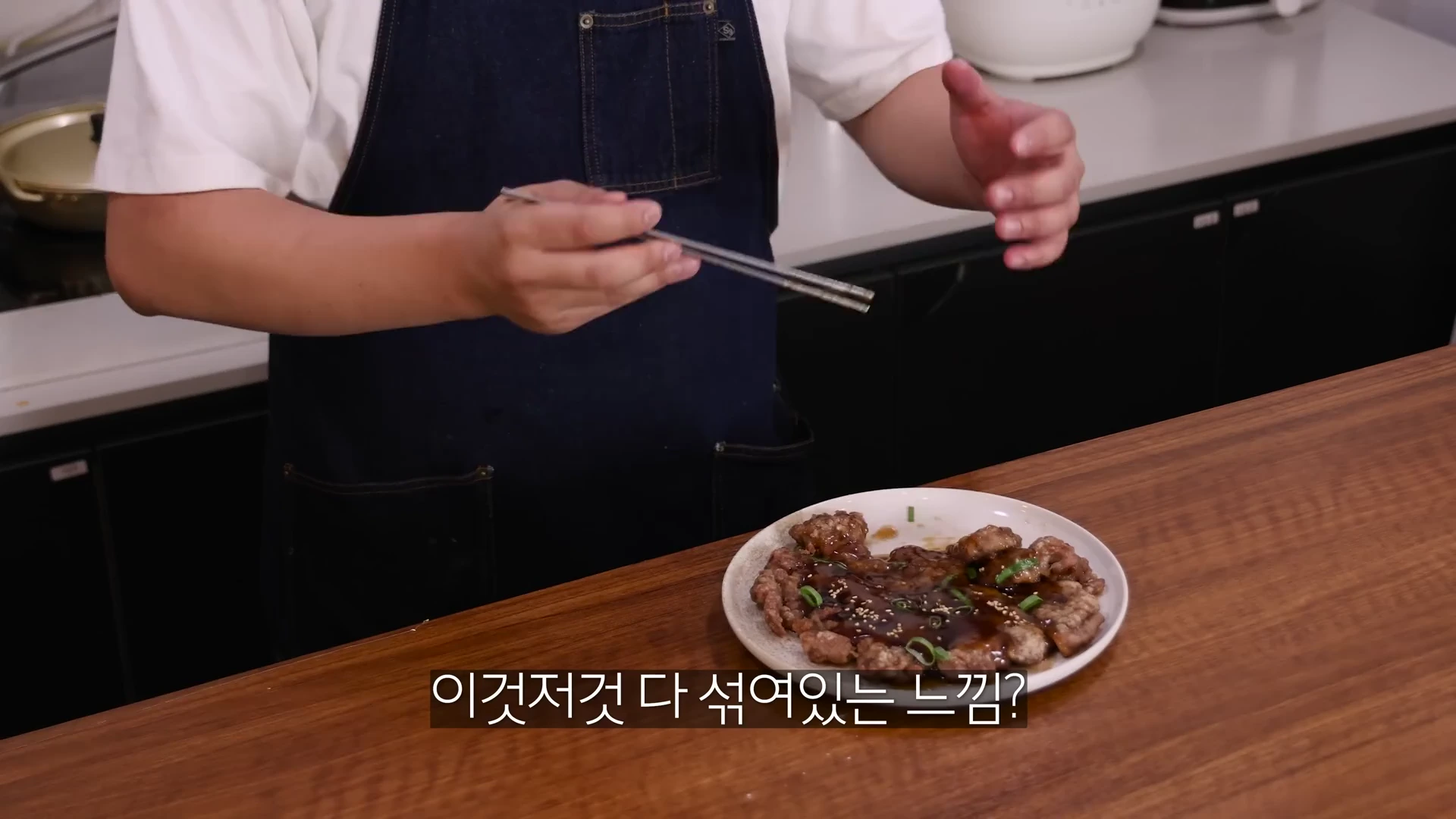 앞치마를 두른 요리사가 접시에 담긴 납작한 탕수육 위에 소스를 뿌리고 젓가락으로 설명하는 모습