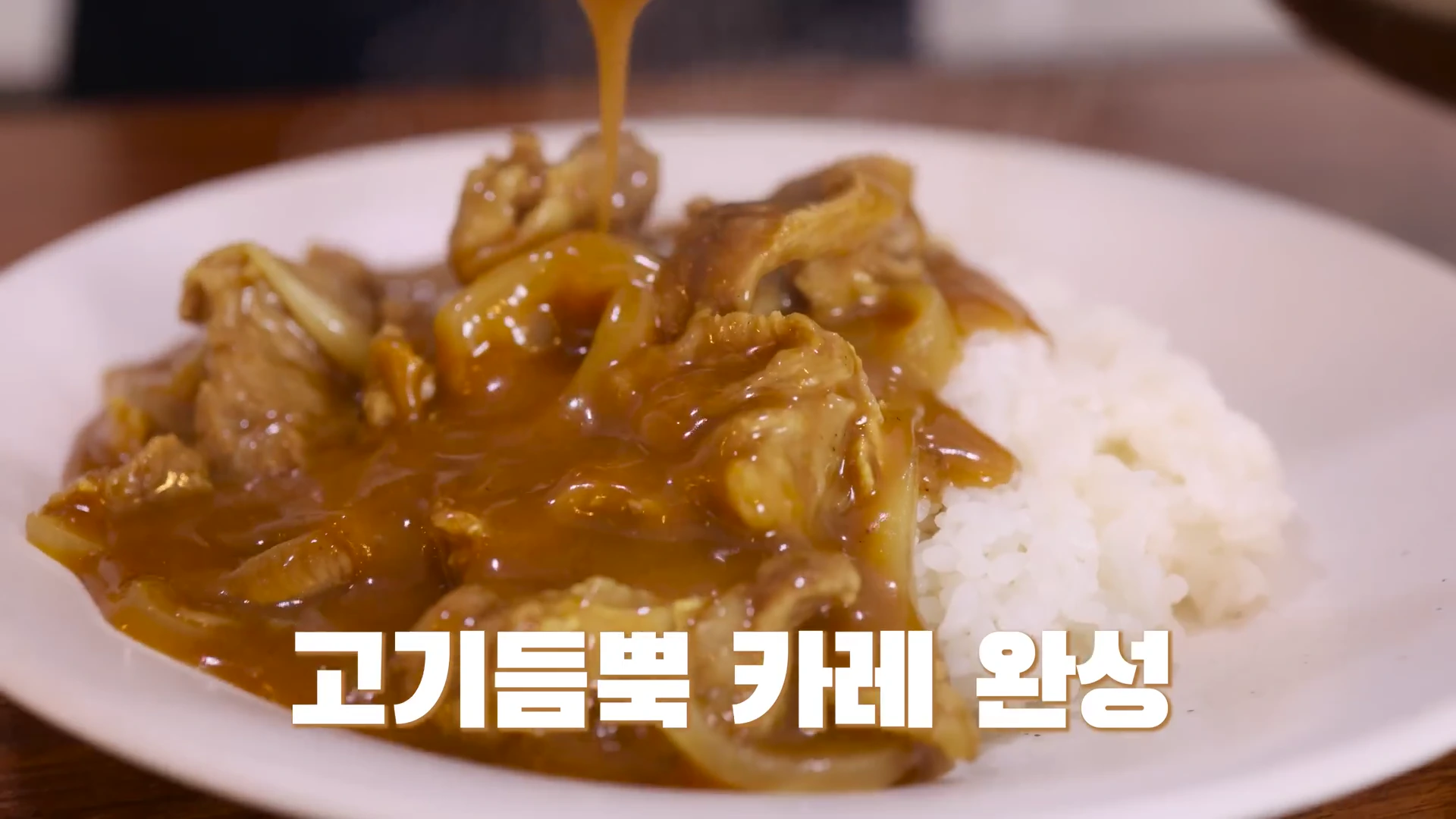 흰 접시에 담긴 밥 위로 걸쭉한 카레 소스가 부어지는 모습이며, 화면 하단에는 고기듬뿍 카레 완성이라는 자막이 적혀 있다.