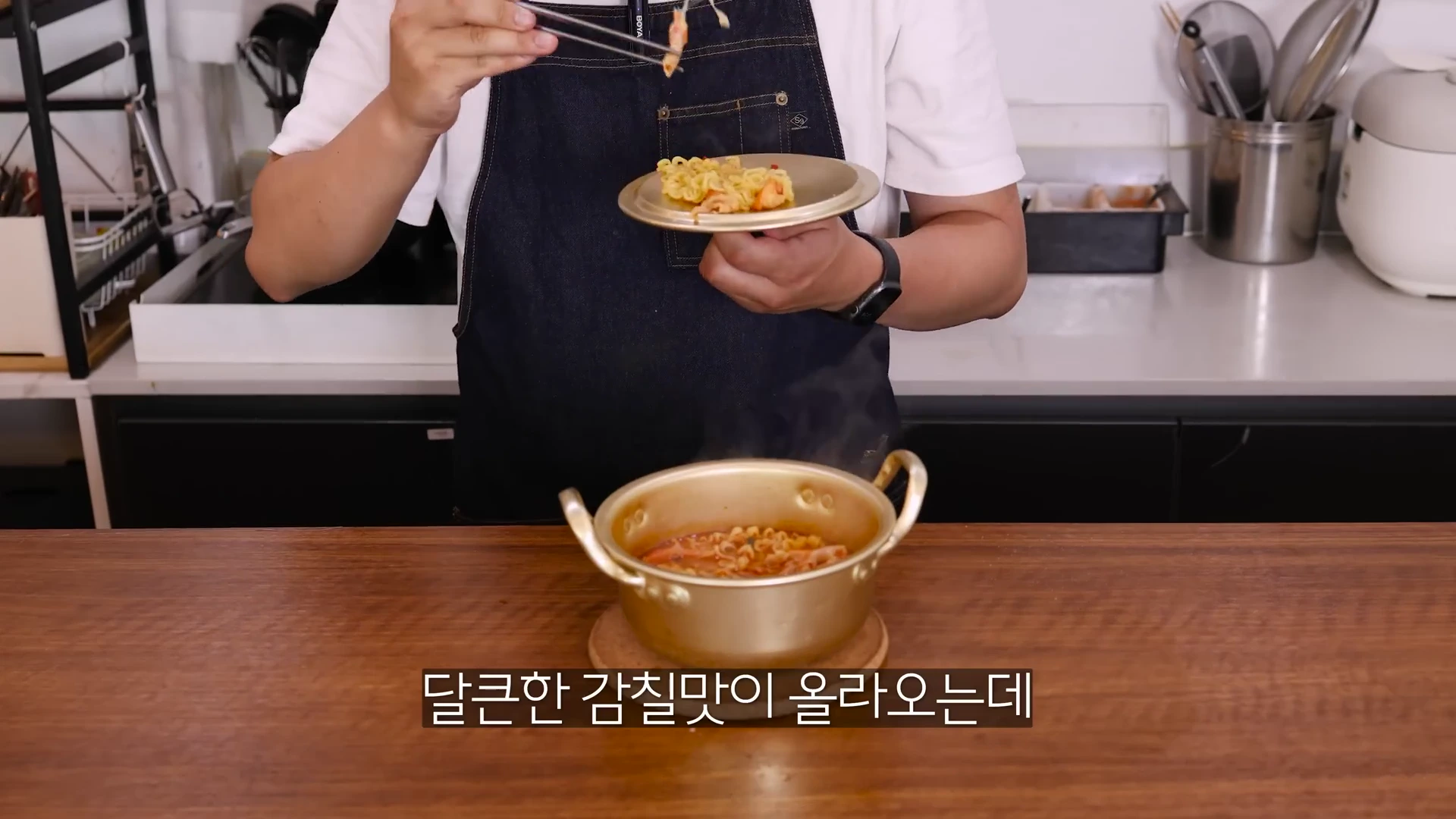 앞치마를 입은 사람이 젓가락으로 대게 살이 들어간 라면을 작은 앞접시에 덜고 있는 모습