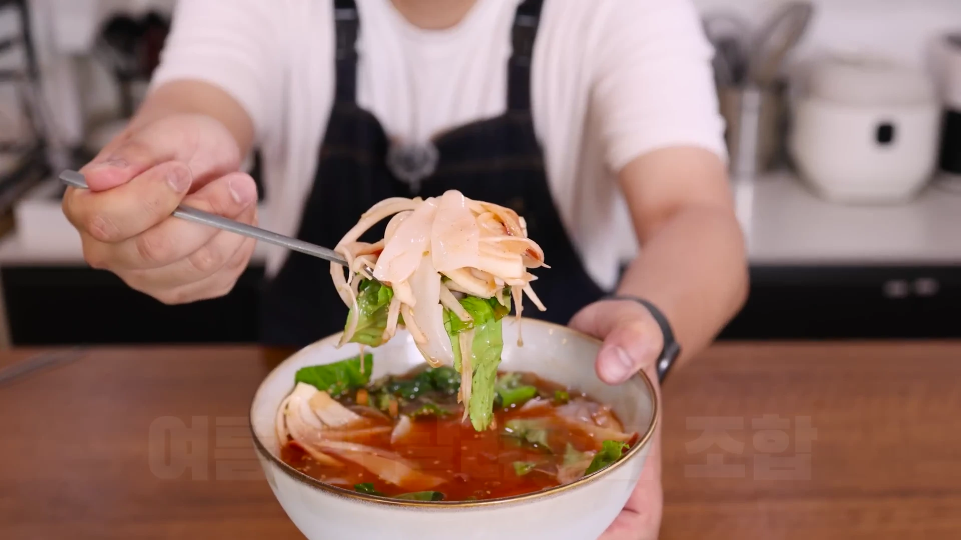 앞치마를 두른 사람이 숟가락으로 회와 야채가 담긴 그릇을 들어 올리고 있는 모습