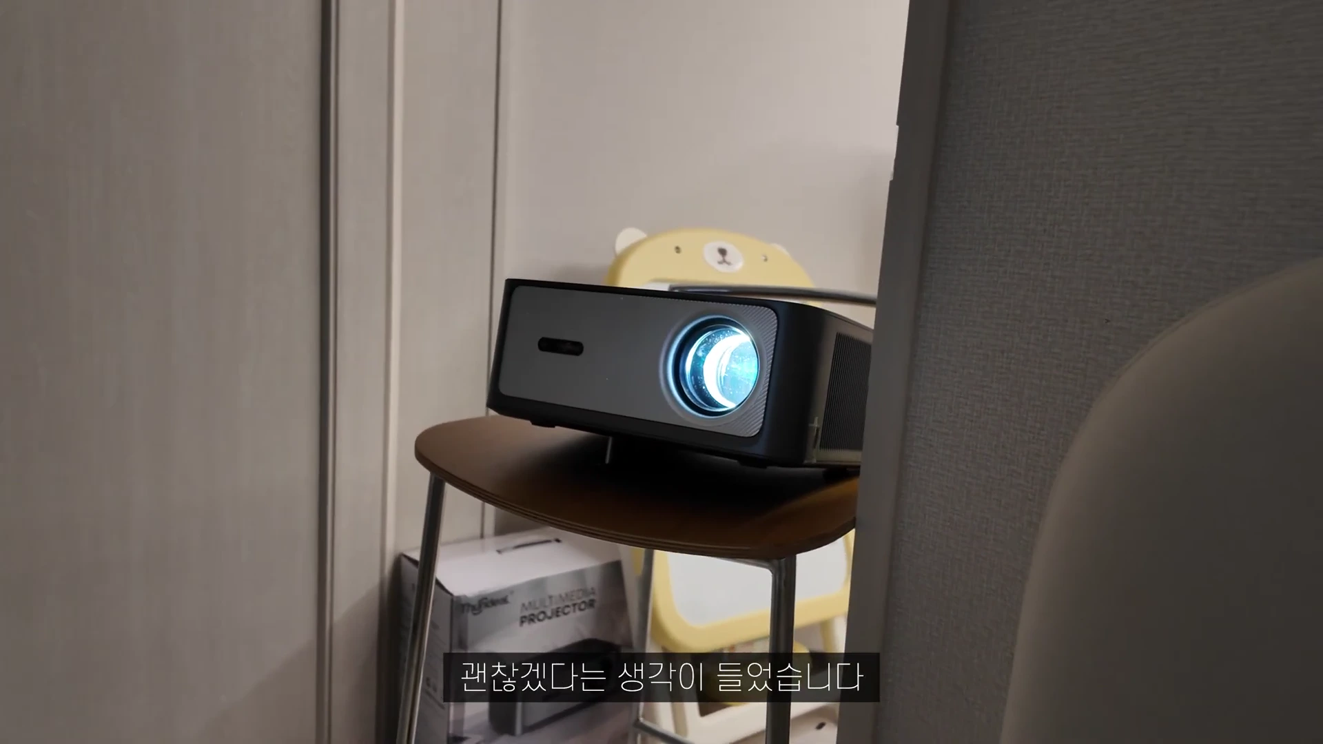 실내에서 나무 의자 위에 놓여 있는 어두운 회색 톤의 빔프로젝터 본체.
