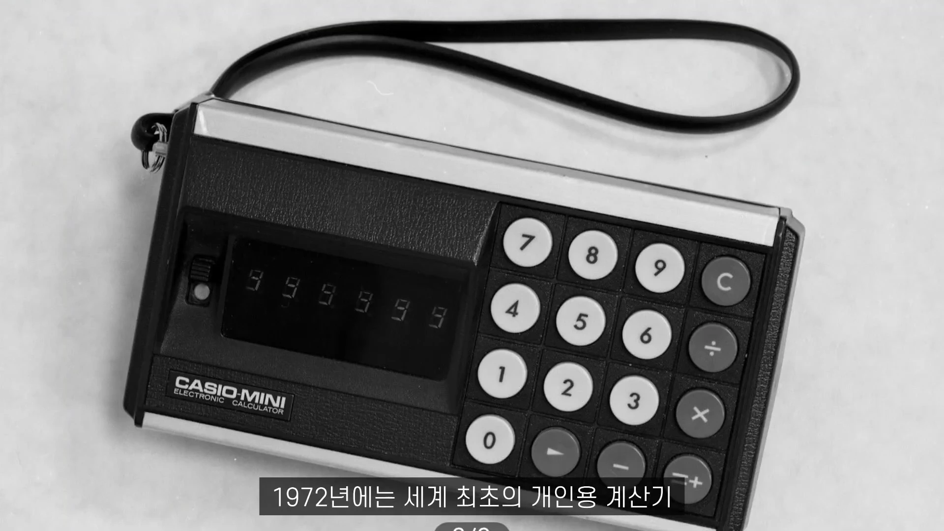 1970년대 빈티지 카시오 미니 전자 계산기가 흰색 배경 위에 놓여 있으며, 화면에는 숫자가 표시되어 있고 아래쪽에는 둥근 버튼들이 배치되어 있다.