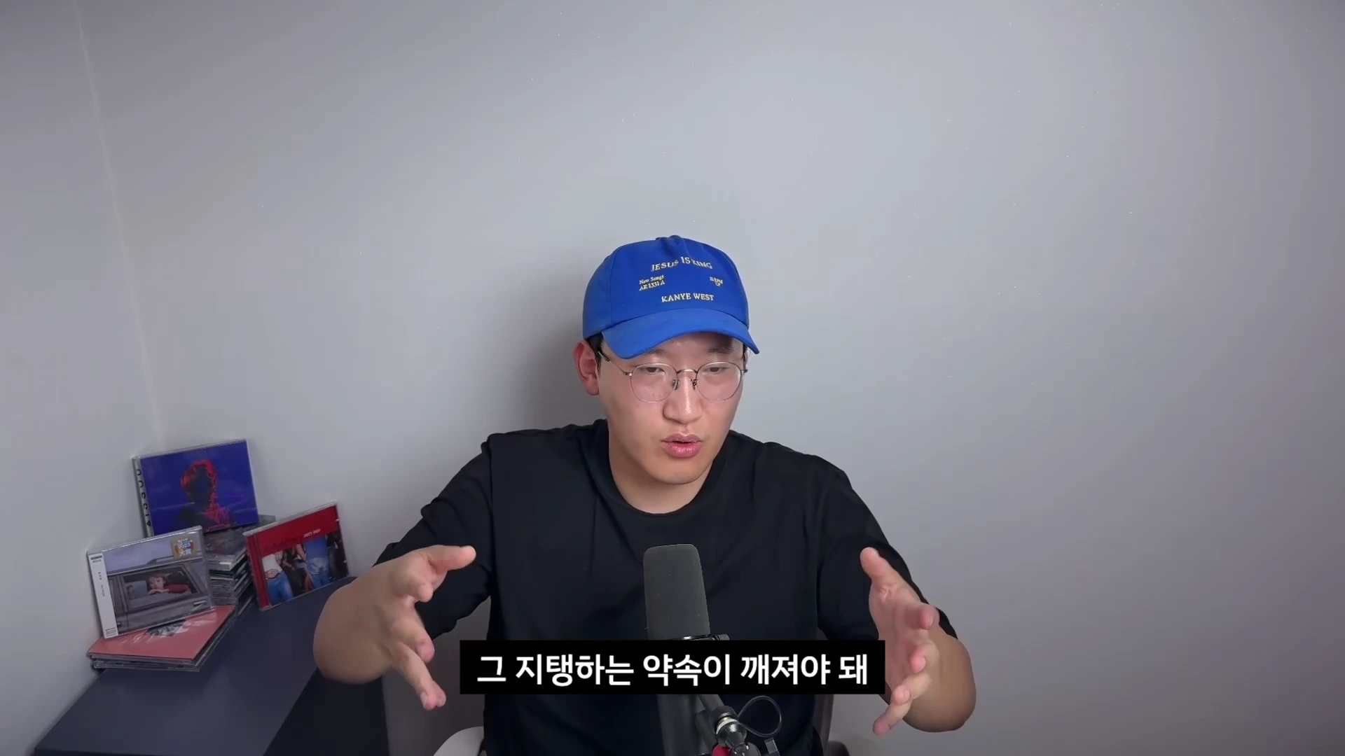 파란색 야구 모자를 쓴 남성이 마이크 앞에서 손을 움직이며 이야기하고 있고, 하단에는 한국어 자막이 표시되어 있습니다.