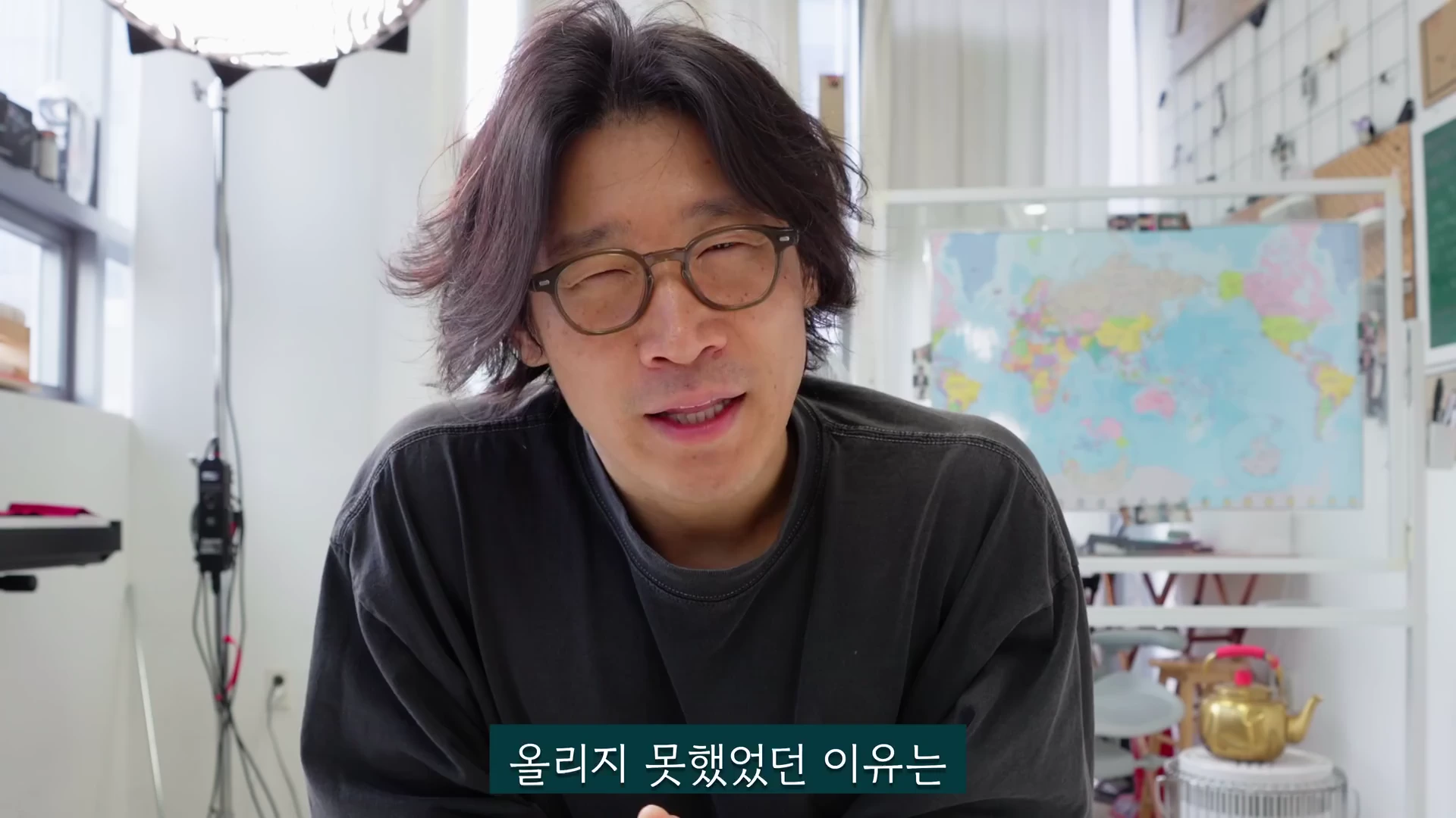 실내에서 안경을 쓴 중년 남성이 카메라를 보며 이야기하고 있고, 하단에는 '올리지 못했었던 이유는'이라는 한국어 자막이 표시되어 있습니다.