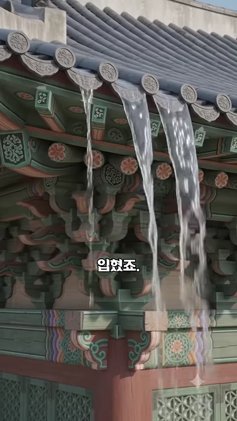 경복궁 근정전의 처마 끝에서 빗물이 가느다란 물줄기가 되어 바닥으로 떨어지는 모습과 함께 정교한 단청이 칠해진 목조 구조가 드러난 화면.
