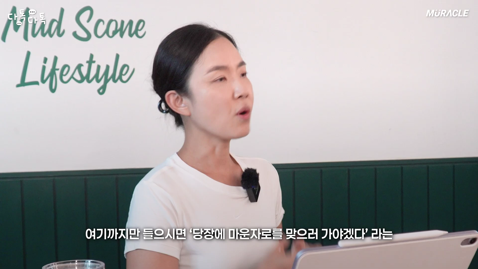 흰색 티셔츠를 입은 여성이 밝은 실내에서 이야기를 나누고 있으며, 하단에는 한국어 자막이 표시되어 있습니다.