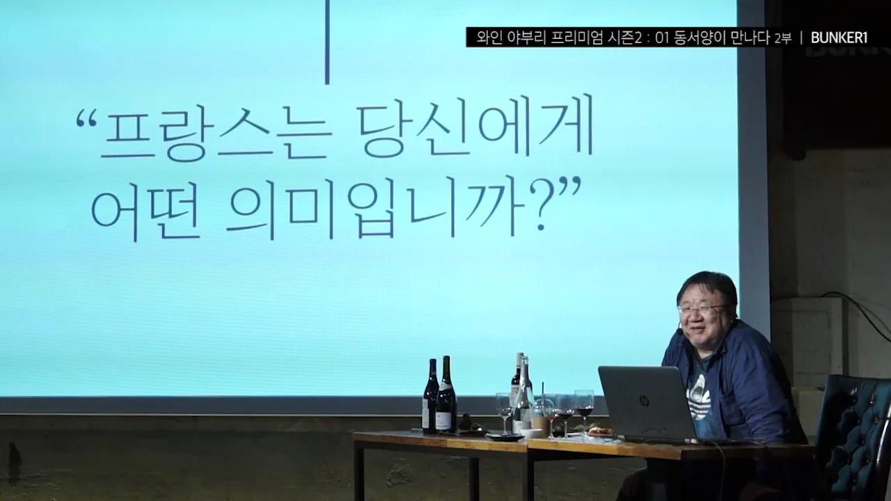 강단에 앉아 노트북을 앞에 두고 강의하는 남성과 그 뒤로 '프랑스는 당신에게 어떤 의미입니까?'라는 문구가 적힌 대형 스크린이 보입니다.