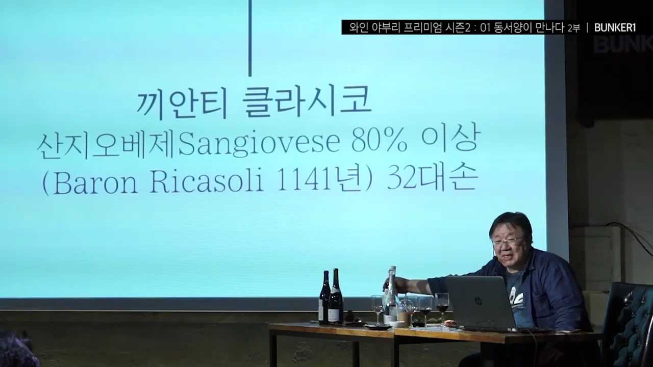 강연자가 화면에 '끼안티 클라시코 산지오베제 80% 이상'이라는 문구가 띄워진 대형 스크린 앞에 앉아 노트북과 와인병을 앞에 두고 청중에게 이야기를 건네고 있다.
