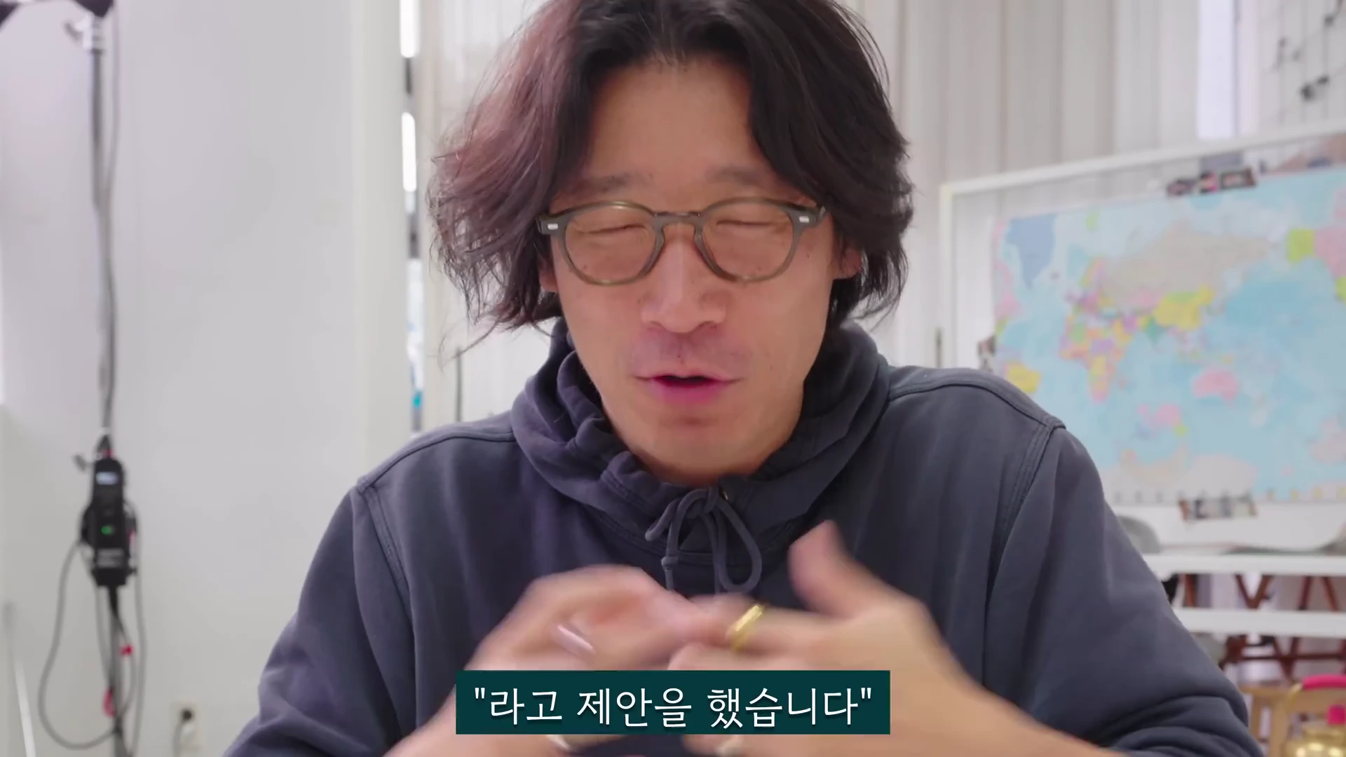 실내에서 후드티를 입은 안경 쓴 남성이 손을 움직이며 이야기하고 있고 하단에는 '라고 제안을 했습니다'라는 한글 자막이 표시된 영상 화면