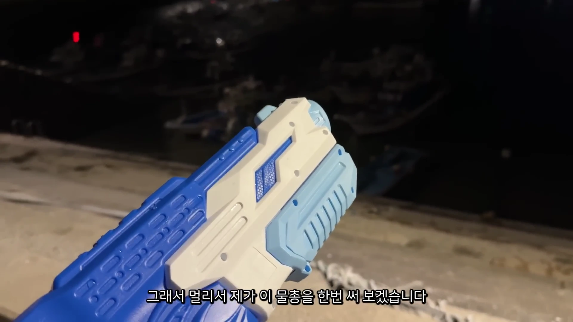 어두운 밤에 파란색과 흰색이 섞인 장난감 물총을 들고 있는 모습.