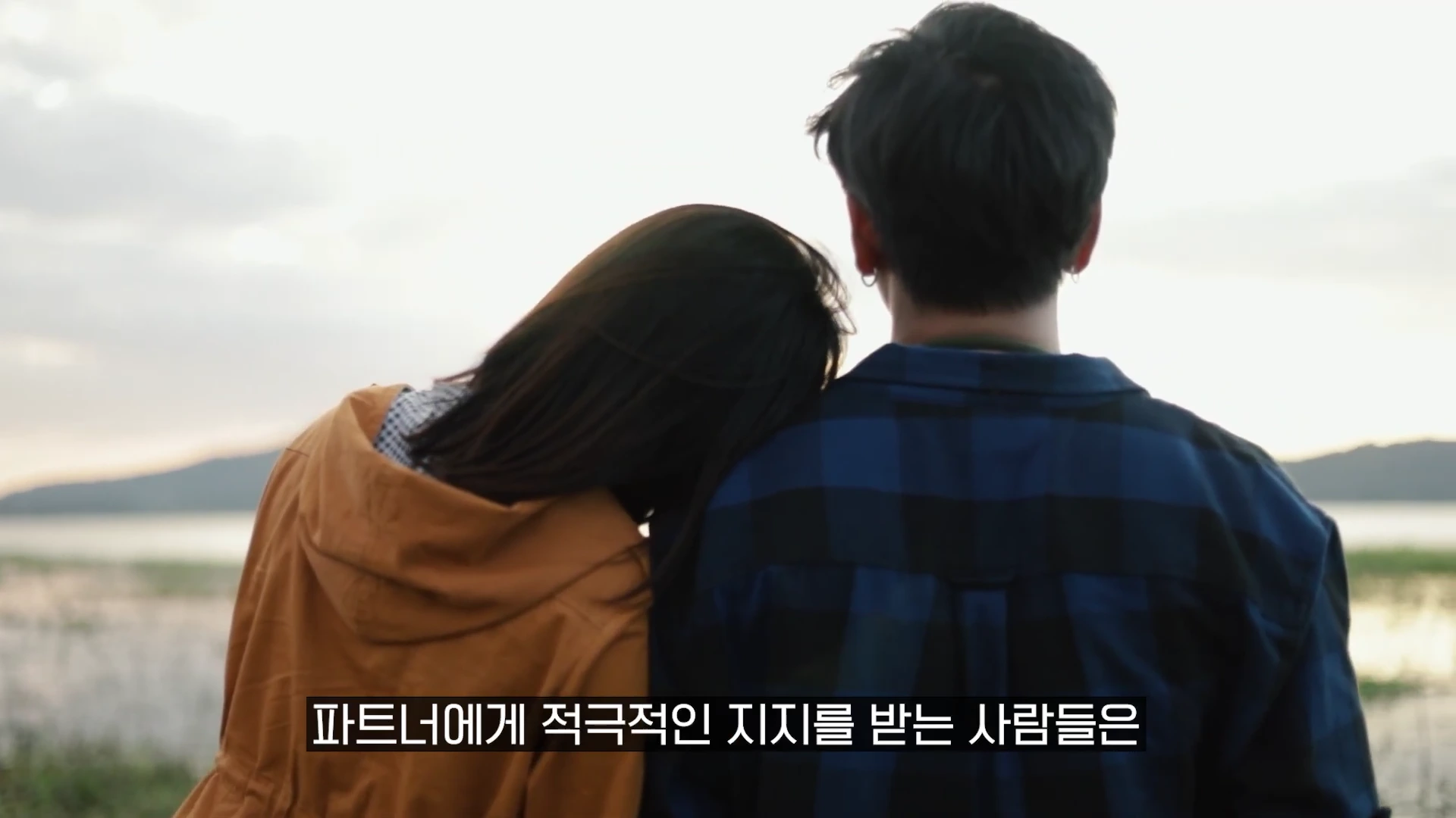 노을이 지는 야외를 배경으로 남녀가 나란히 앉아 서로 기대어 있는 뒷모습