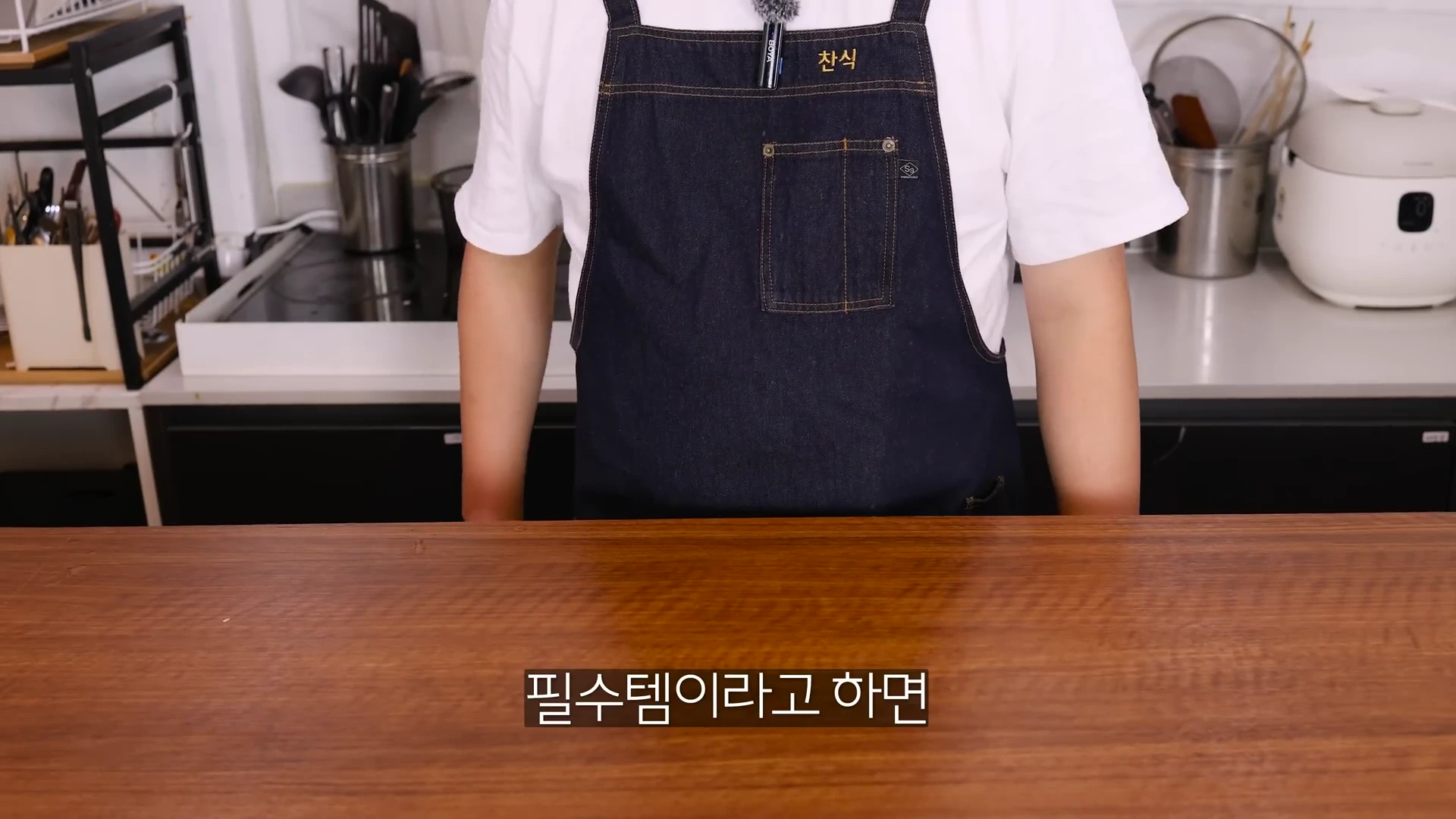 앞치마를 입은 요리사가 주방 조리대 앞에 서 있고 화면 하단에 '필수템이라고 하면'이라는 자막이 떠 있다.