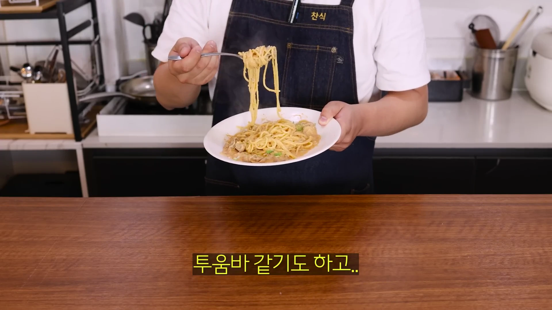 앞치마를 두른 사람이 완성된 크림 파스타가 담긴 접시를 들고 포크로 면을 들어 올리고 있으며, 화면 하단에 '투움바같기도 하고..'라는 자막이 보입니다.