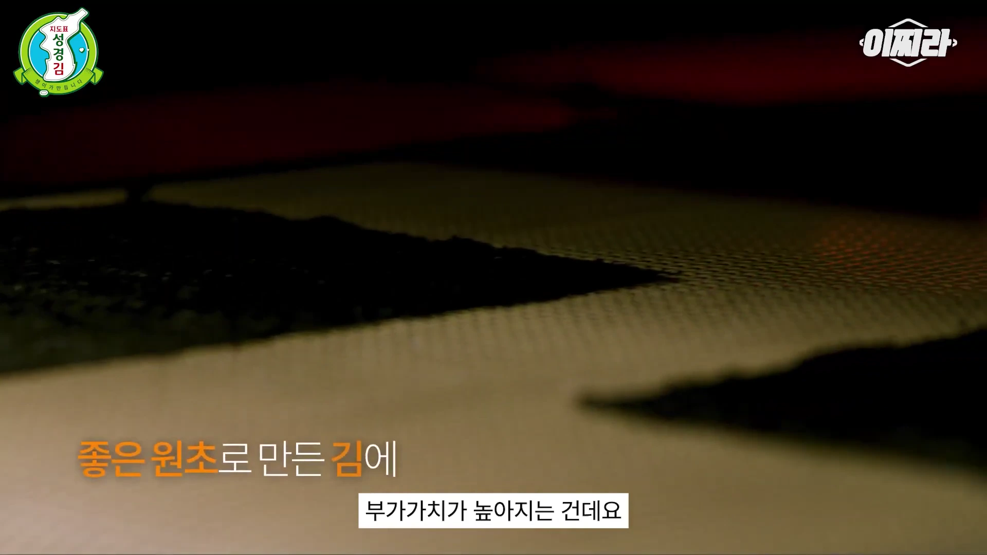 어두운 배경 속에서 컨베이어 벨트를 지나가는 김의 모습과 함께 '좋은 원초로 만든 김에 부가가치가 높아지는 건데요'라는 자막이 하단에 표시된 영상 화면.