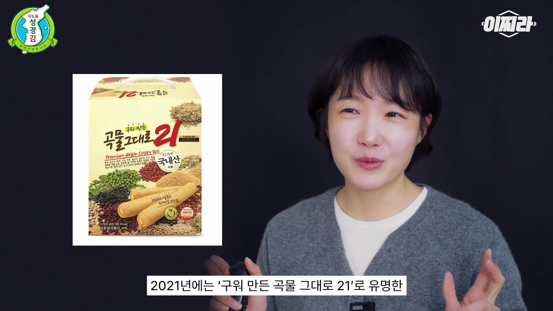 단발머리의 여성 진행자가 스튜디오에서 설명하고 있으며 화면 왼쪽에는 '구워 만든 곡물 그대로 21' 과자 상자 이미지가 배치되어 있습니다.