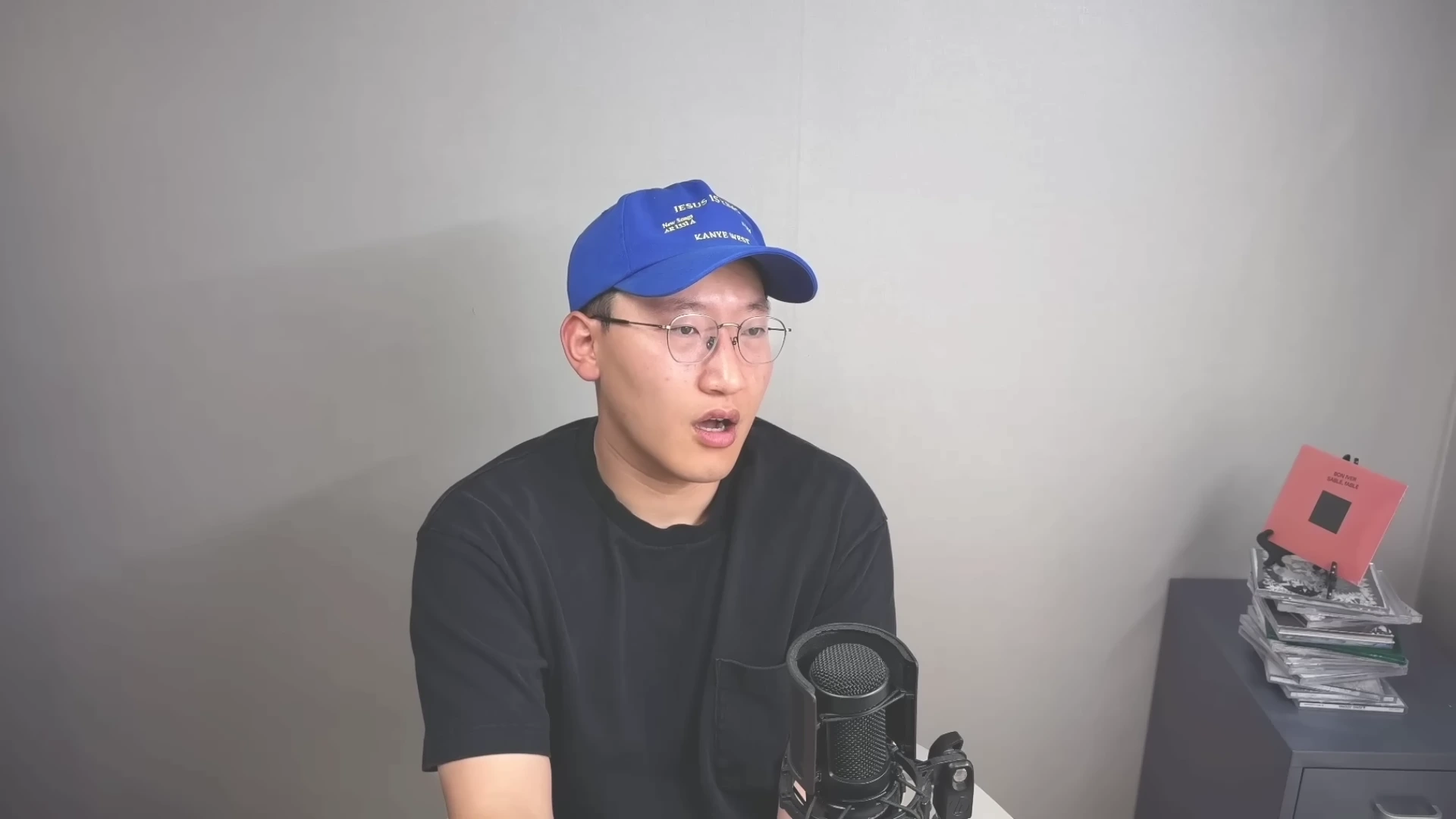 파란색 모자를 쓰고 검은색 티셔츠를 입은 남성이 마이크 앞에서 이야기하고 있다.