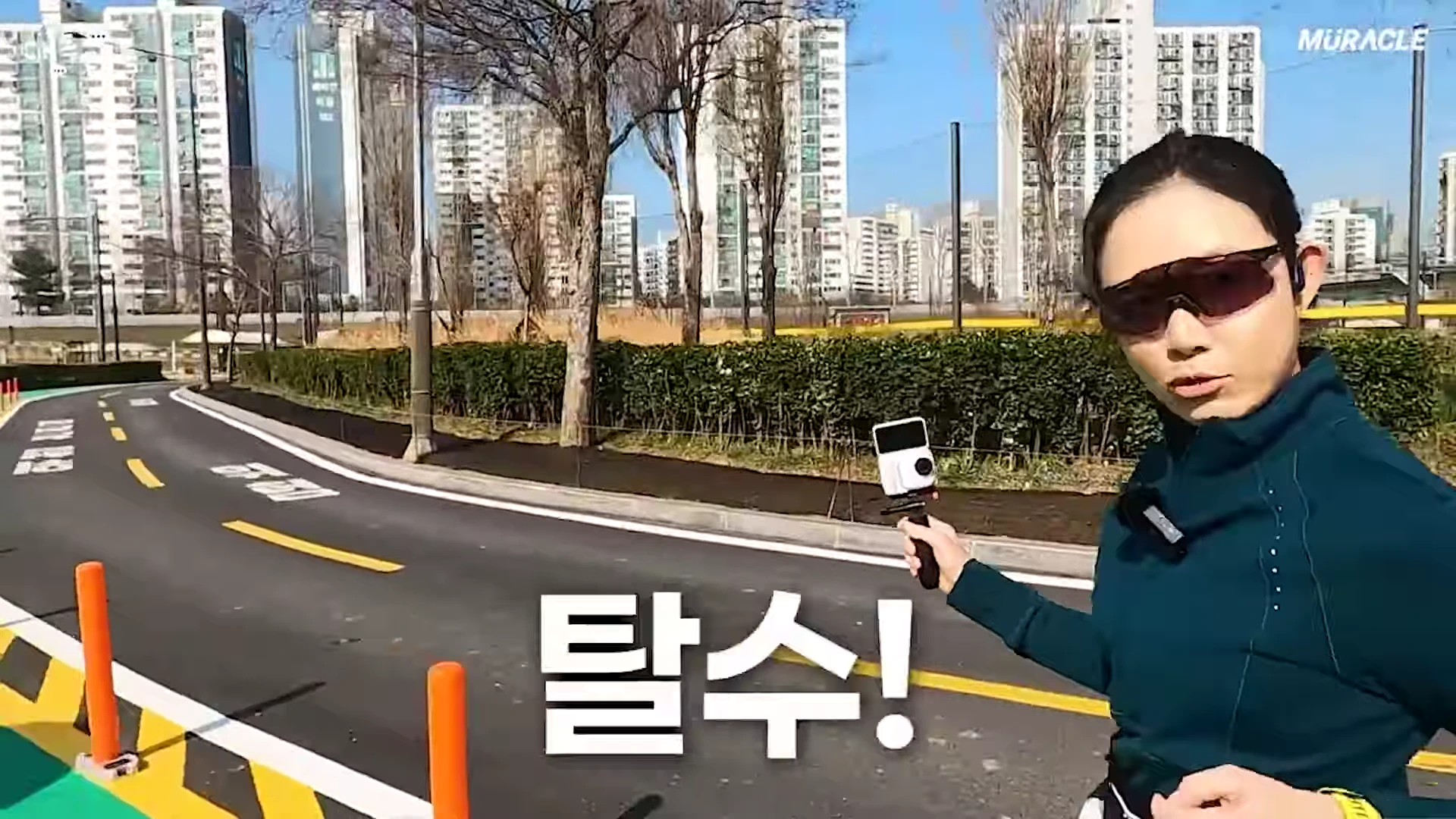 러닝 복장을 한 여성이 야외 도로에서 카메라를 들고 걸으며 이야기하고 있고, 화면 중앙에 '탈수!'라는 큰 글자가 떠 있습니다.