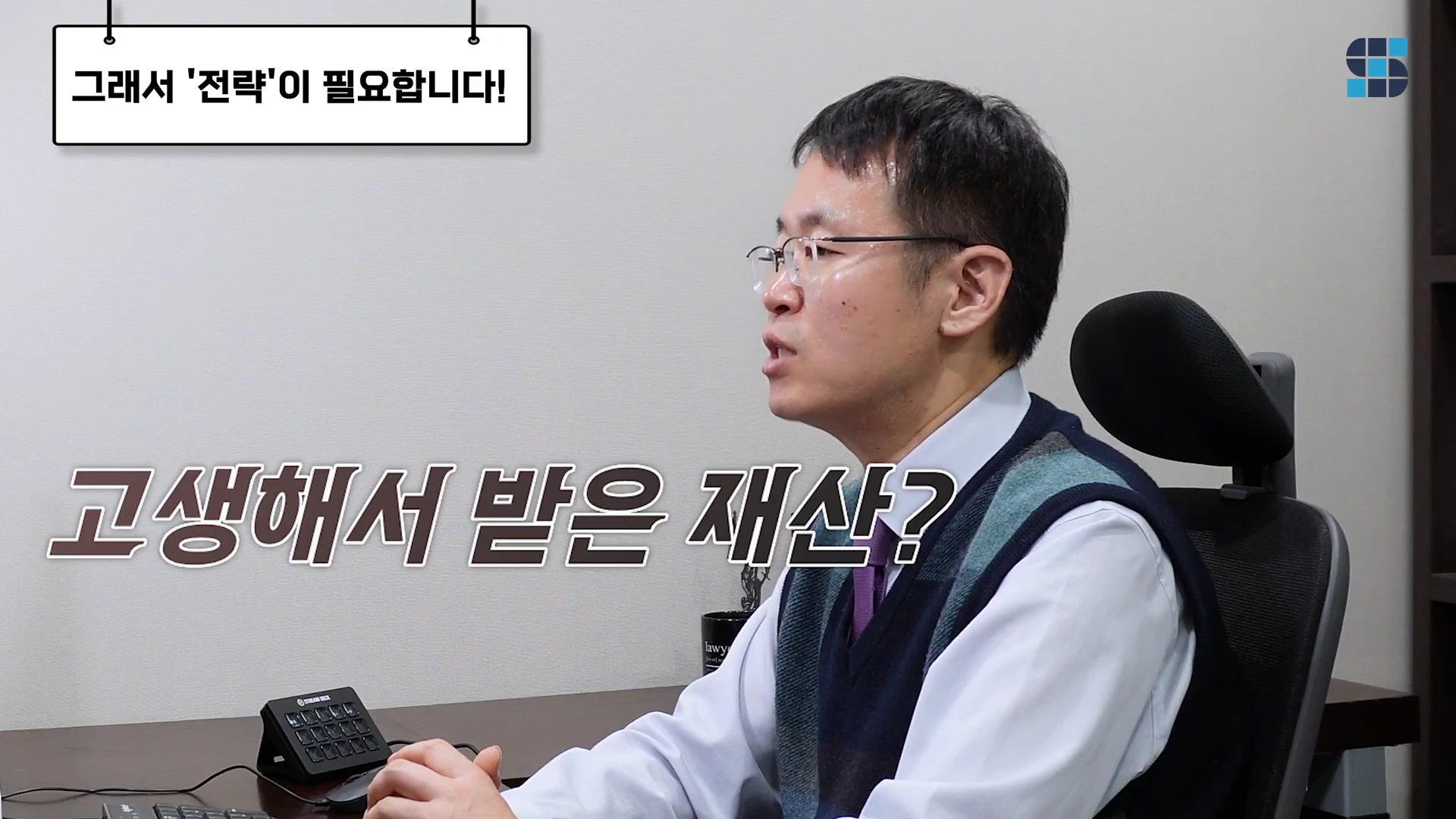 안경을 쓴 남성이 사무실 책상에 앉아 이야기하는 모습이 담긴 영상 캡처 화면이며, 화면 상단에는 '그래서 전략이 필요합니다!'라는 문구와 중앙에는 '고생해서 받은 재산?'이라는 큰 자막이 배치되어 있다.