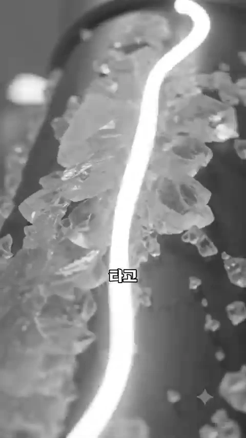 검은색 절연체 표면에 달라붙은 투명한 얼음 결정체들과 그 옆으로 흐르는 밝은 빛줄기가 근접 촬영된 영상.