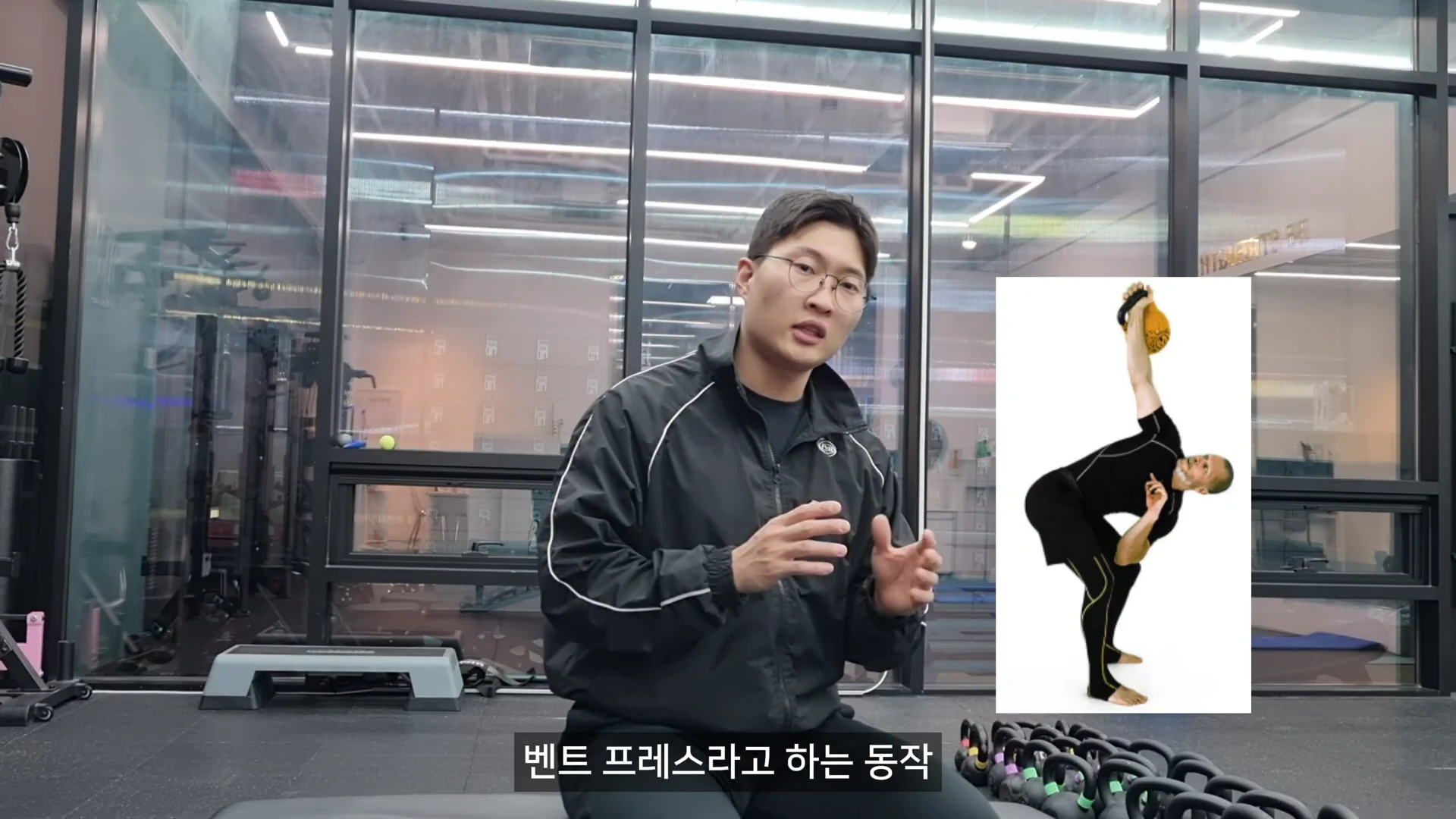 체육관을 배경으로 안경을 쓴 남성이 앉아서 설명하고 있고, 화면 오른쪽에는 케틀벨을 들고 벤트 프레스 동작을 수행하는 운동인의 이미지가 삽입되어 있다.