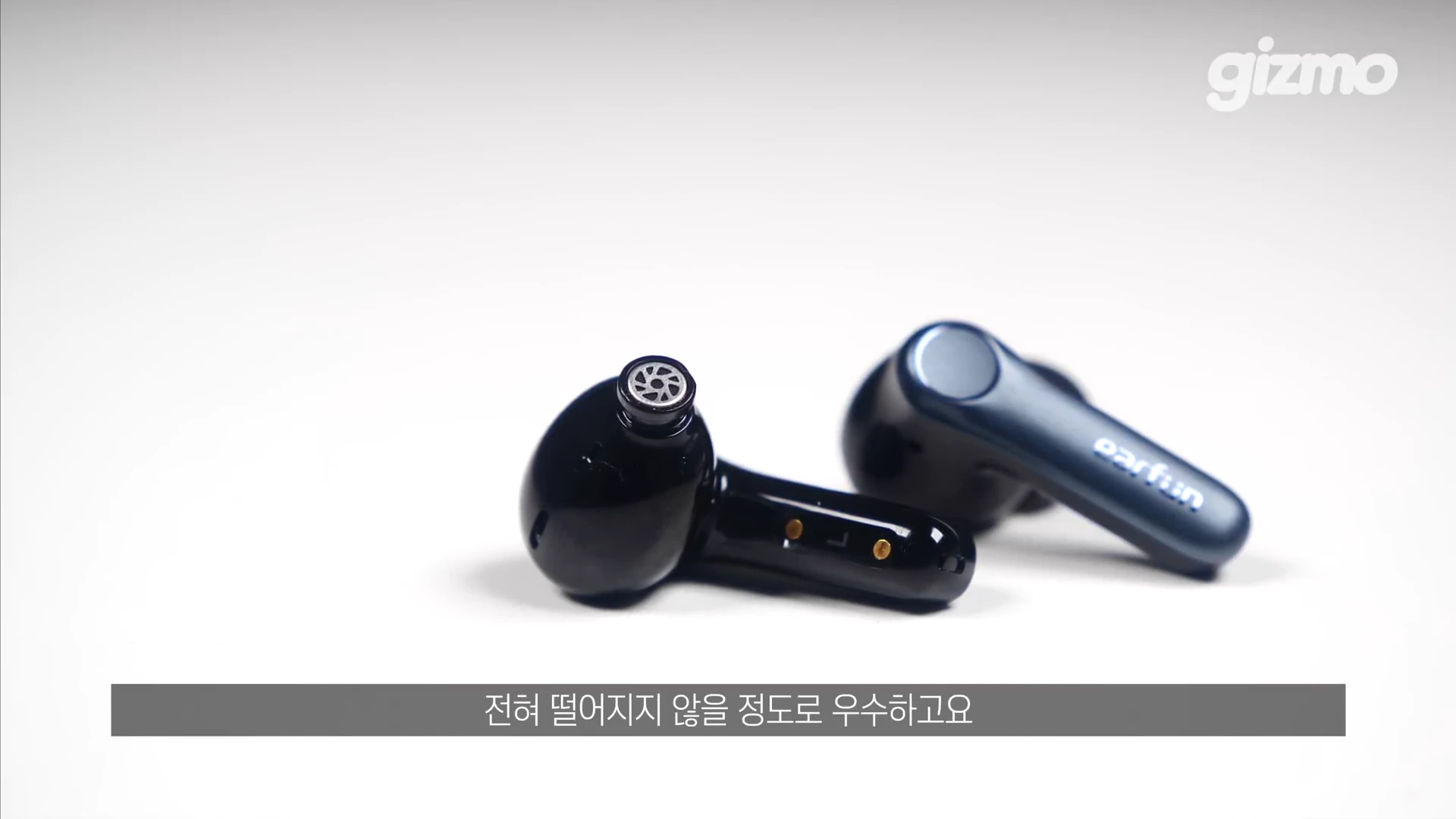 흰색 배경 위에 놓인 검은색 무선 이어폰 한 쌍과 그 위에 자막이 표시된 영상 화면