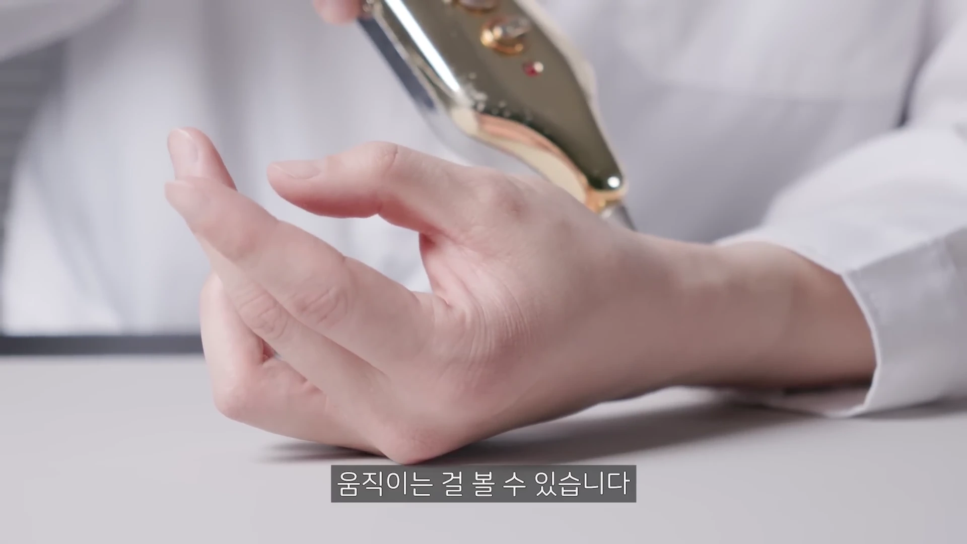 흰색 가운을 입은 사람의 손등 위에 EMS 전기 자극 기기를 대고 있는 모습입니다.