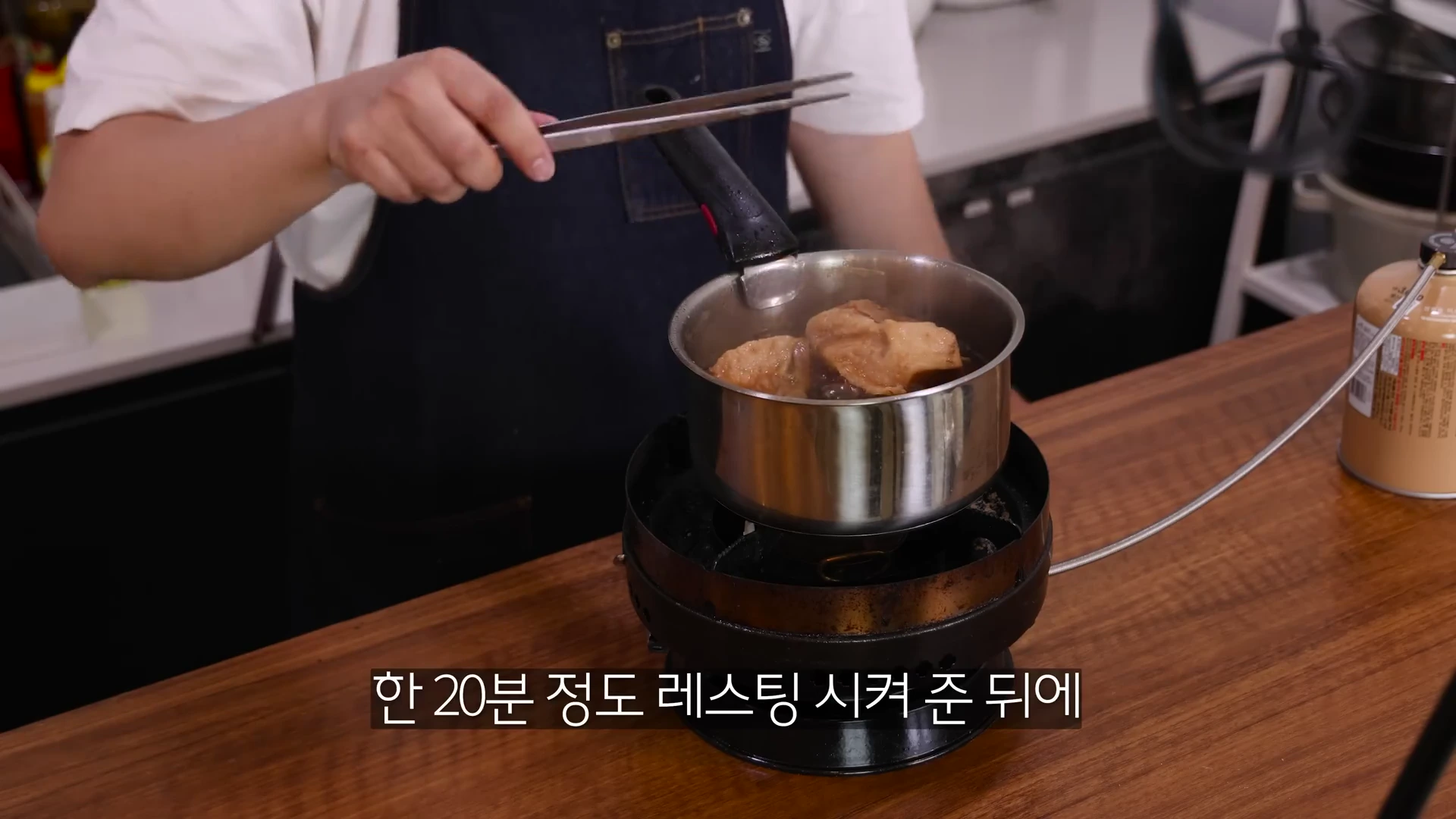 앞치마를 두른 요리사가 냄비 속의 고기를 집게로 들어 올리고 있는 모습