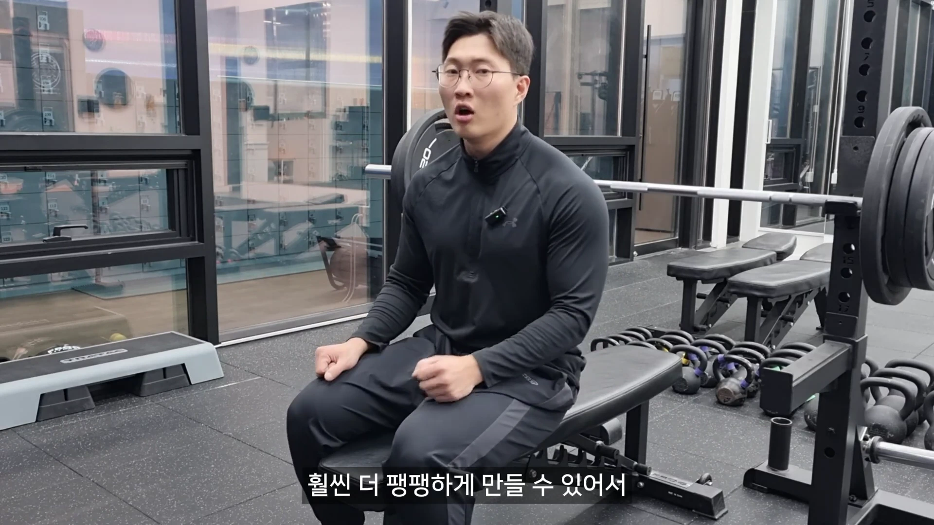 체육관에서 안경을 쓴 남성이 운동용 벤치에 앉아 상체를 꼿꼿이 세우고 설명하는 모습.