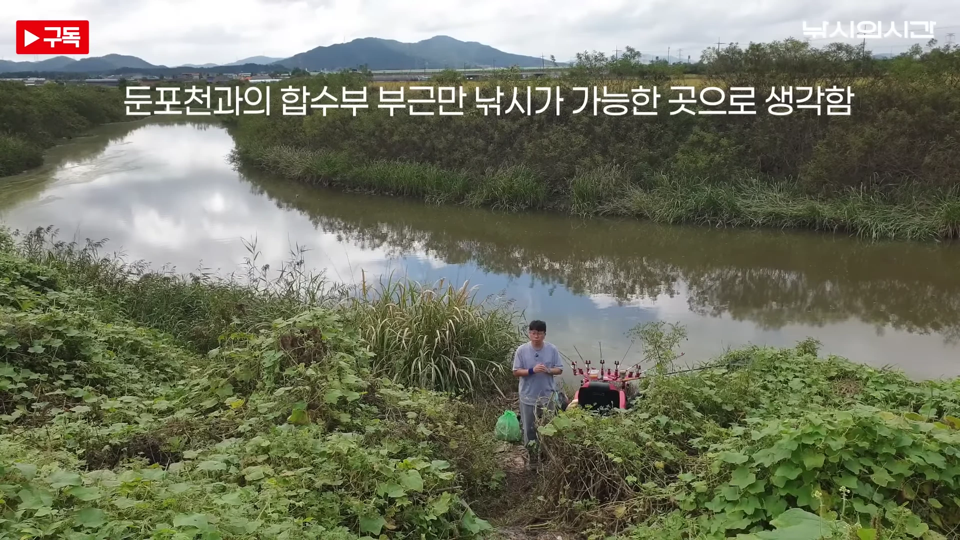 한 남성이 낚시 장비가 설치된 풀이 무성한 수로가에서 서서 이야기하고 있고, 화면 상단에는 '둔포천과의 합수부 부근만 낚시가 가능한 곳으로 생각함'이라는 자막이 떠 있습니다.