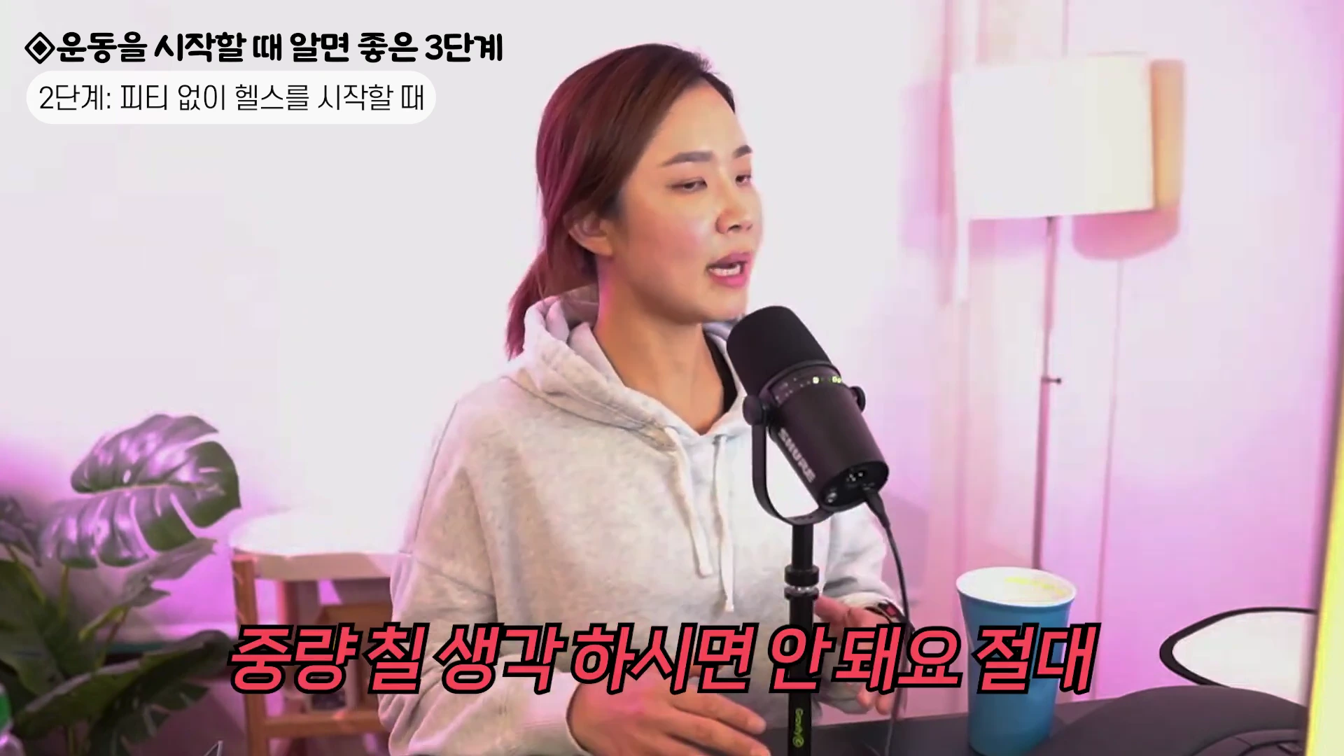 실내 스튜디오에서 회색 후드티를 입은 여성이 검은색 마이크를 앞에 두고 이야기하고 있으며 화면 상단에는 '운동을 시작할 때 알면 좋은 3단계'라는 텍스트가 표시되어 있습니다.