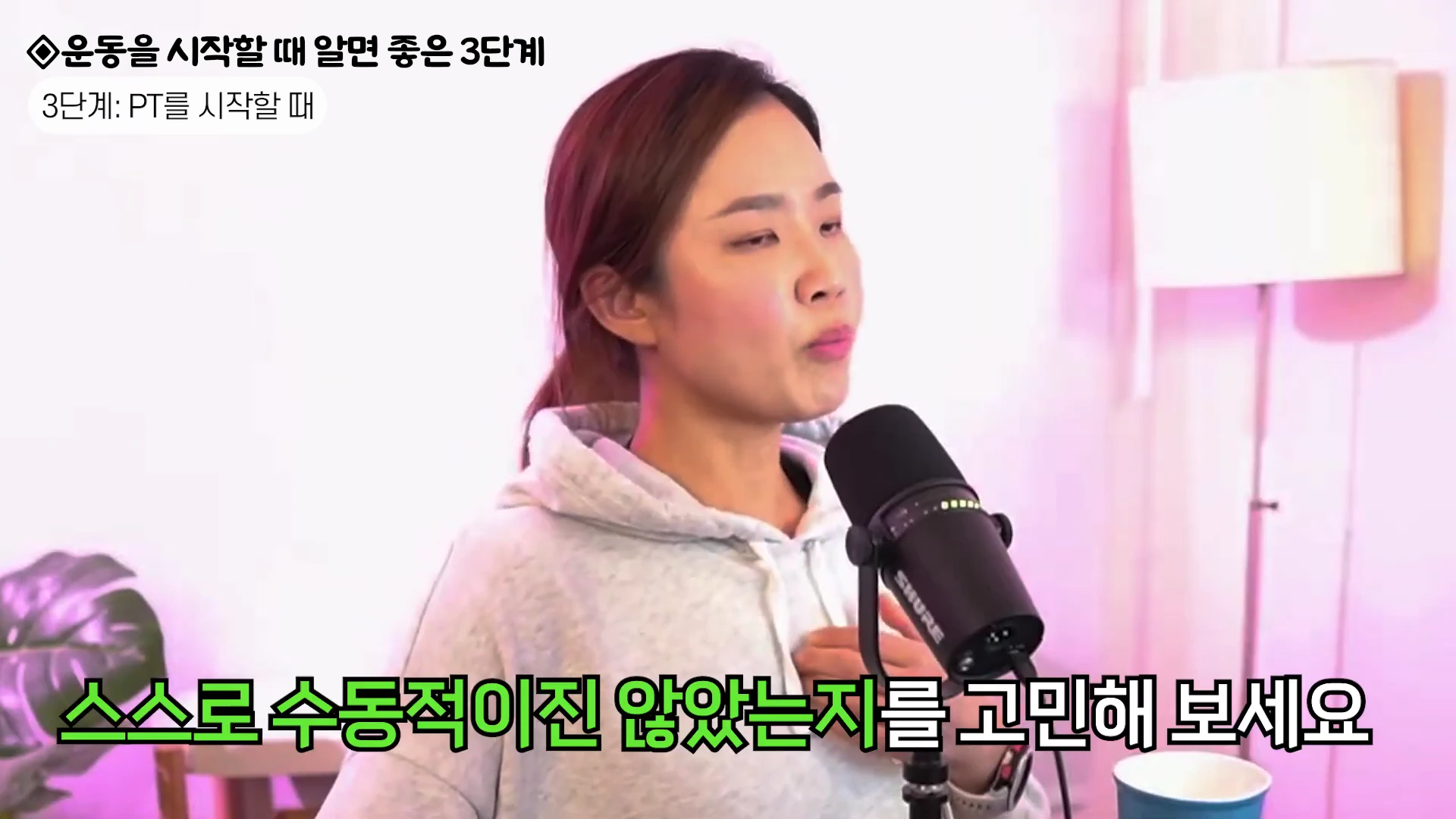 실내 스튜디오에서 후드티를 입은 여성이 마이크 앞에 앉아 이야기를 하고 있으며, 화면 상단과 하단에는 운동 관련 텍스트가 자막으로 표시되어 있습니다.
