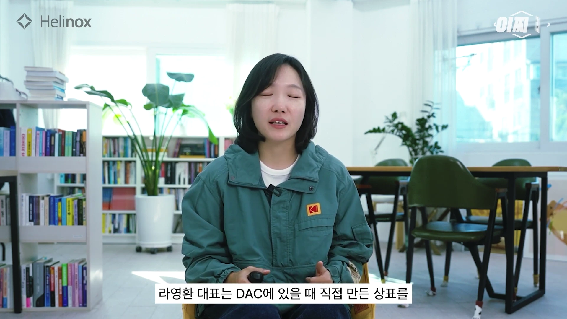밝은 실내를 배경으로 어깨너머에 책장과 화분이 배치된 공간에서 한 여성이 앉아 이야기를 나누고 있는 모습입니다.