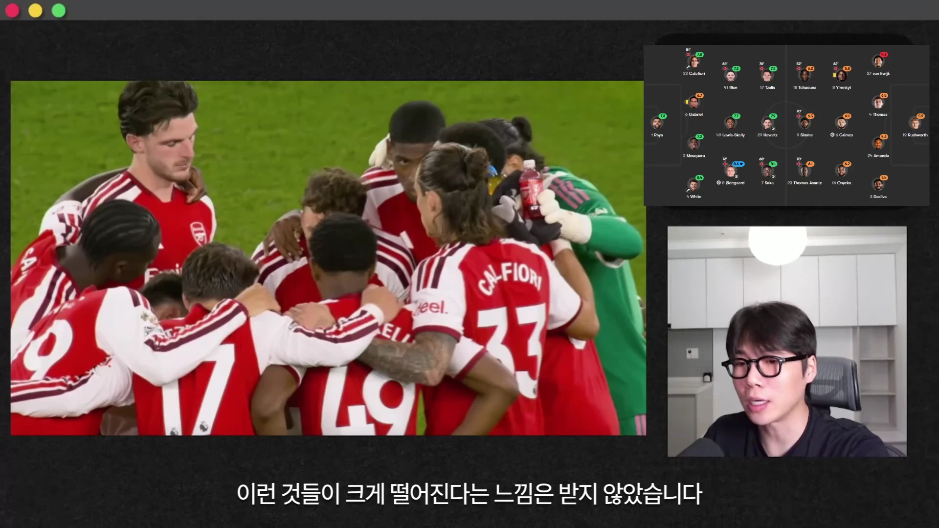 붉은색 유니폼을 입은 축구 선수들이 경기장 위에서 서로 어깨를 맞대고 모여 있는 모습과, 화면 오른쪽 상단에 경기 포메이션 및 평점 그래픽이 표시되어 있으며, 하단에는 안경을 쓴 진행자가 이야기하는 모습이 영상 프레임 안에 함께 담겨 있습니다.