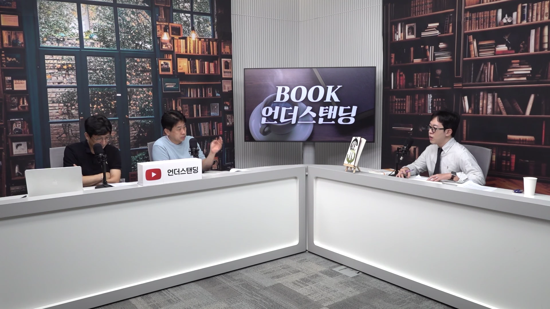 두 명의 남성이 서재 배경의 스튜디오에서 책상에 앉아 마이크를 앞에 두고 대화를 나누고 있으며, 뒤편 화면에는 'BOOK 언더스탠딩' 로고가 떠 있습니다.