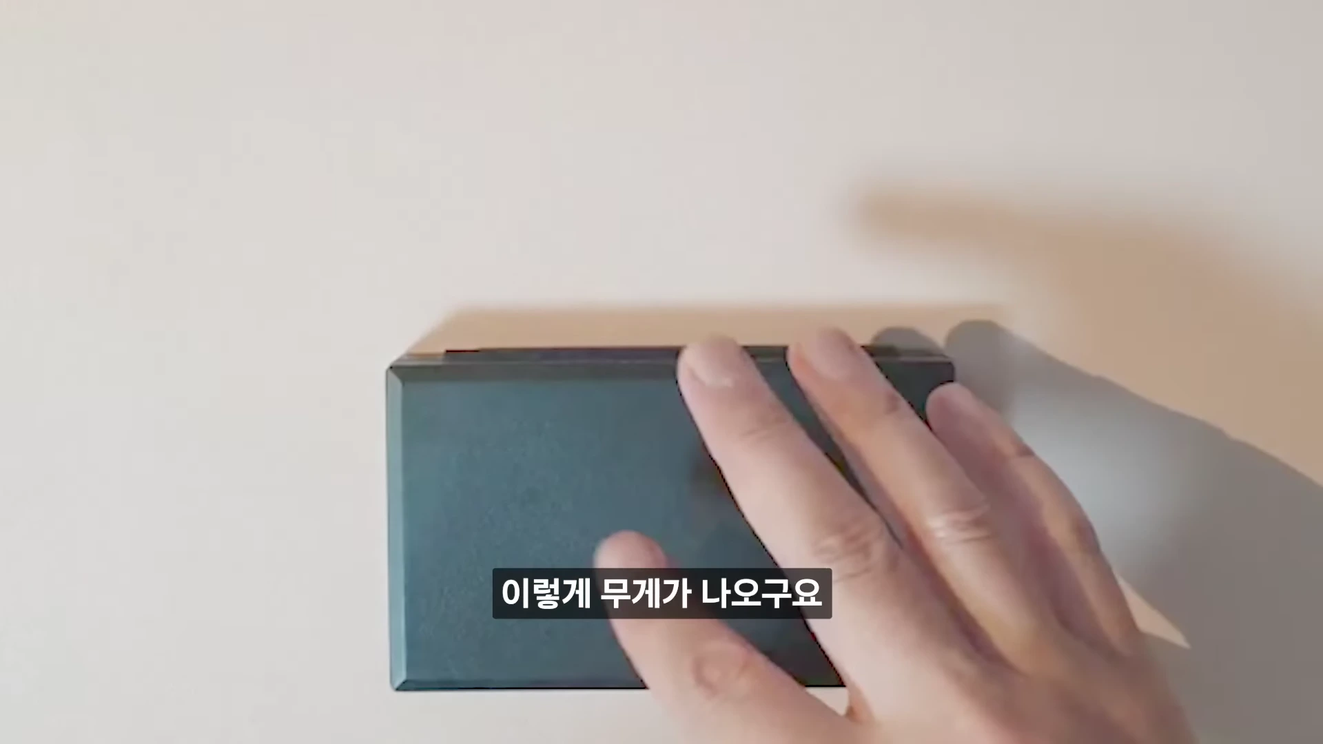 사람의 손이 디지털 저울 위에 놓인 낚싯대를 가볍게 누르며 무게를 측정하는 모습이 담긴 영상 캡처 화면입니다.