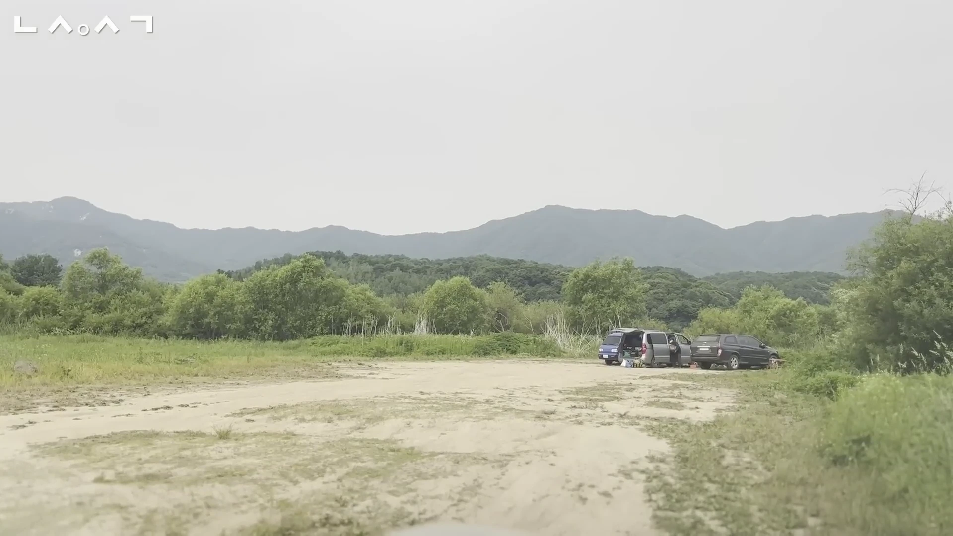 강원도 화천의 간척천 주변으로 차들이 주차된 흙길과 푸른 산이 펼쳐진 풍경
