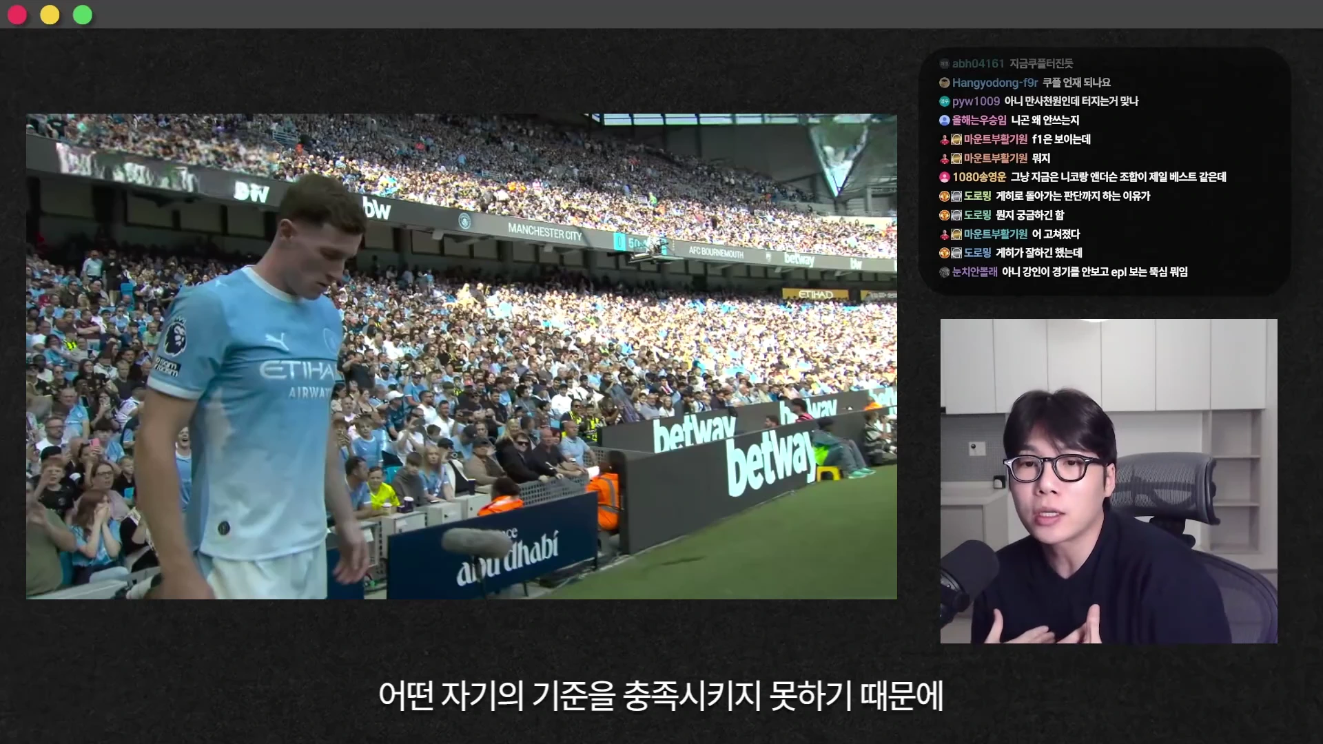 축구 경기 중계 화면 옆에서 안경을 쓴 남성이 마이크를 앞에 두고 이야기를 나누는 라이브 방송 영상 캡처 화면입니다.