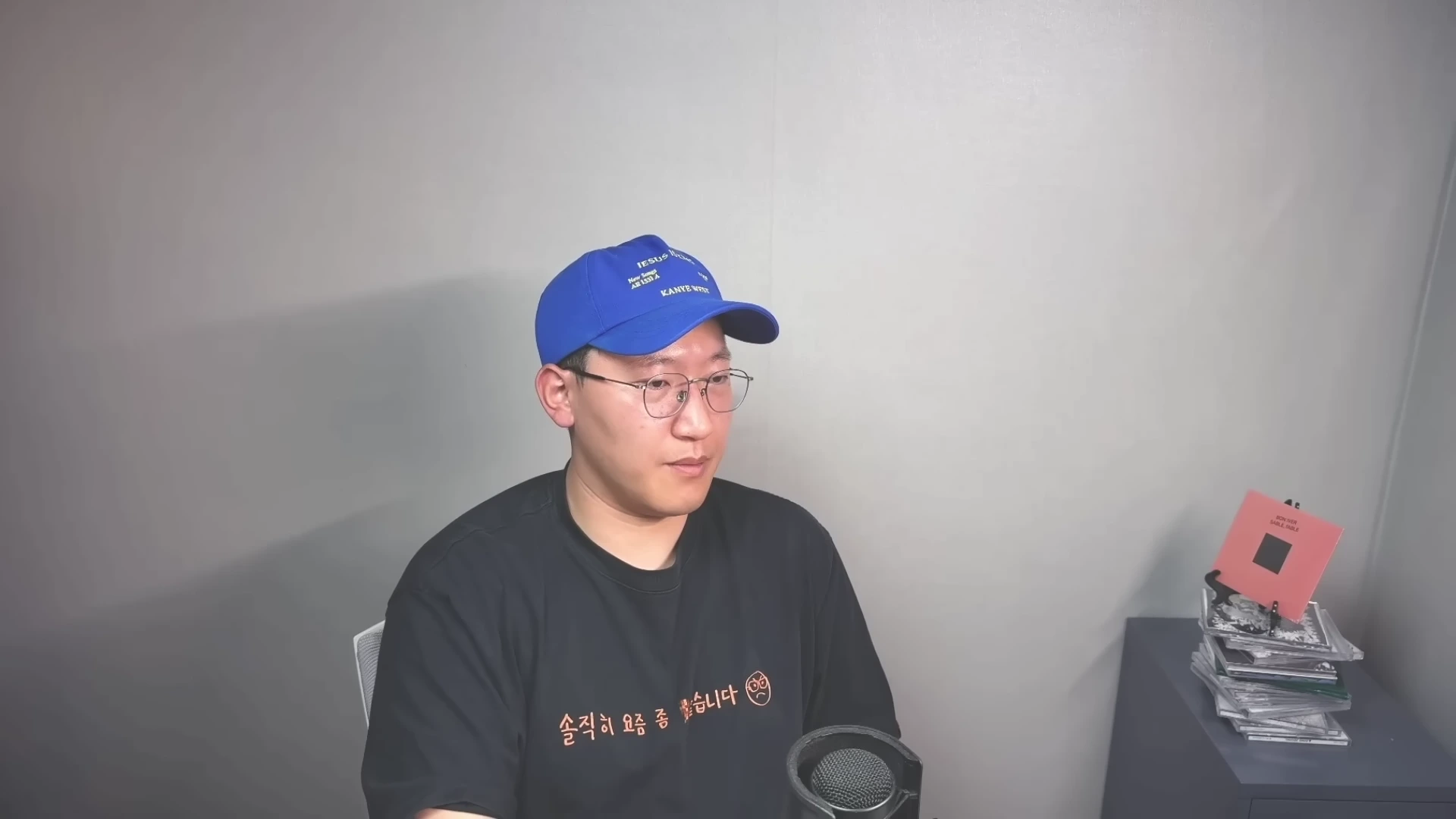파란색 야구 모자와 안경을 쓴 남성이 마이크 앞에서 방송하고 있는 모습