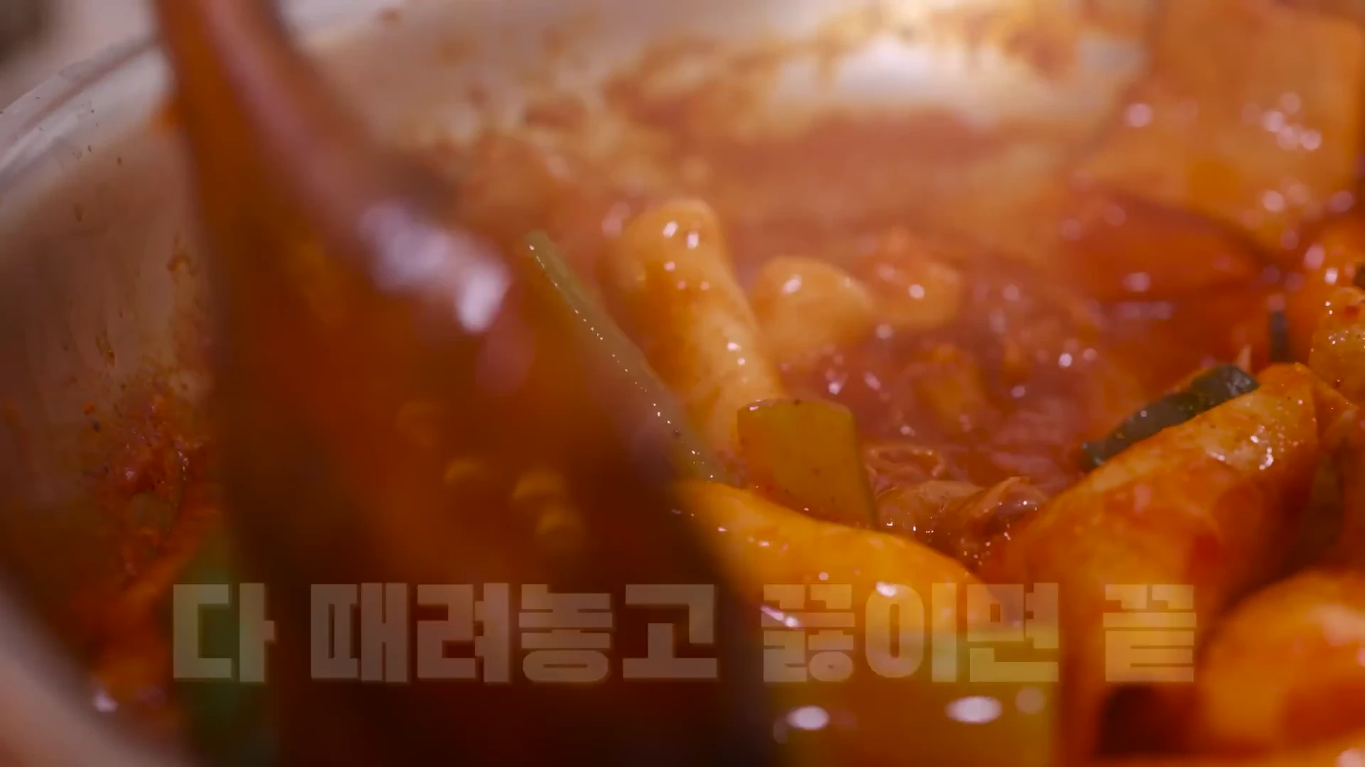냄비 안에서 붉은 양념과 함께 어묵, 떡, 대파가 보글보글 끓고 있는 모습과 이를 나무 주걱으로 젓고 있는 장면을 담은 영상 캡처 화면입니다.