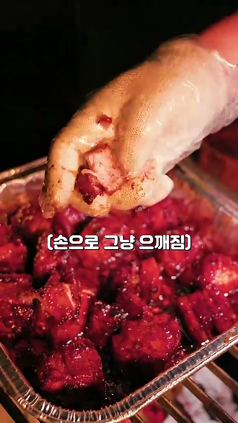 비닐장갑을 낀 손이 조리가 완료된 바베큐 고기 조각을 부드럽게 으깨고 있는 모습