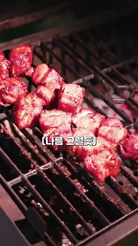 그릴 위에 놓여 노릇하게 익어가고 있는 깍둑썰기한 삼겹살 조각들과 그 위에 덧씌워진 자막