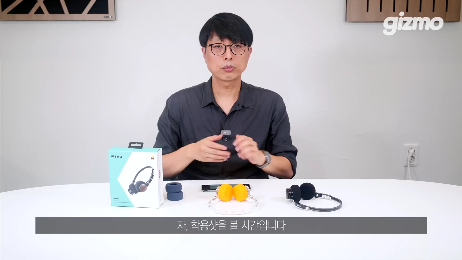 한 남성이 스튜디오 테이블에 앉아 피오 헤드폰 패키지와 헤드폰을 앞에 두고 설명하고 있는 모습