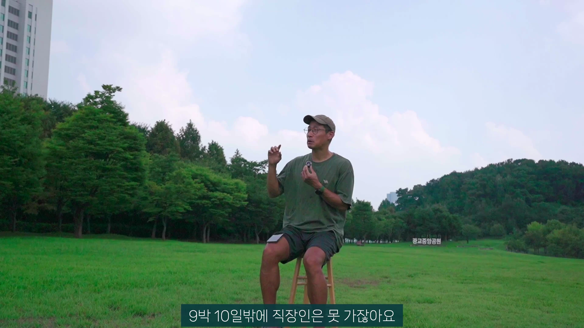 모자와 안경을 쓴 남성이 초록색 잔디밭 위 의자에 앉아 이야기를 하고 있는 모습.