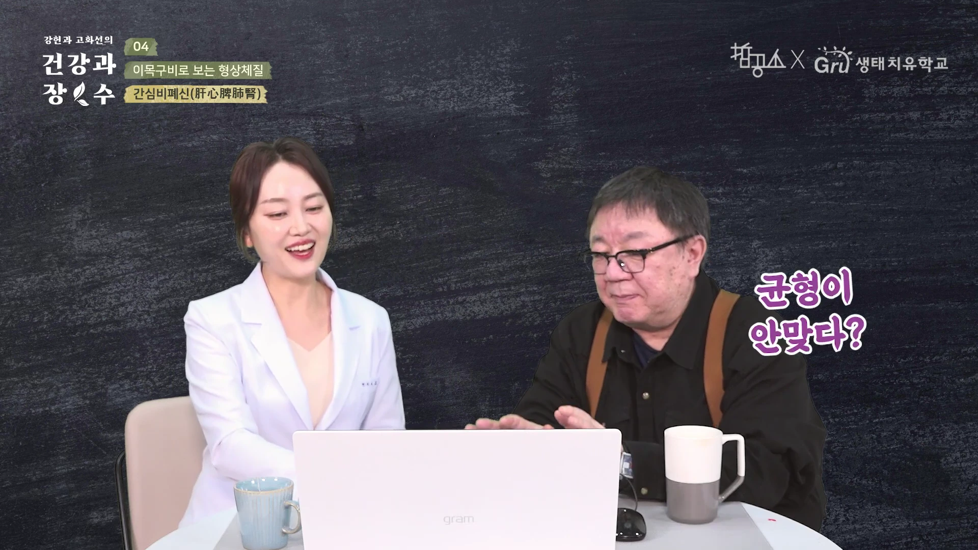 흰색 가운을 입은 여성과 검은색 셔츠를 입은 남성이 테이블 앞에 앉아 노트북 화면을 함께 보며 대화하고 있는 스튜디오 촬영 장면입니다.