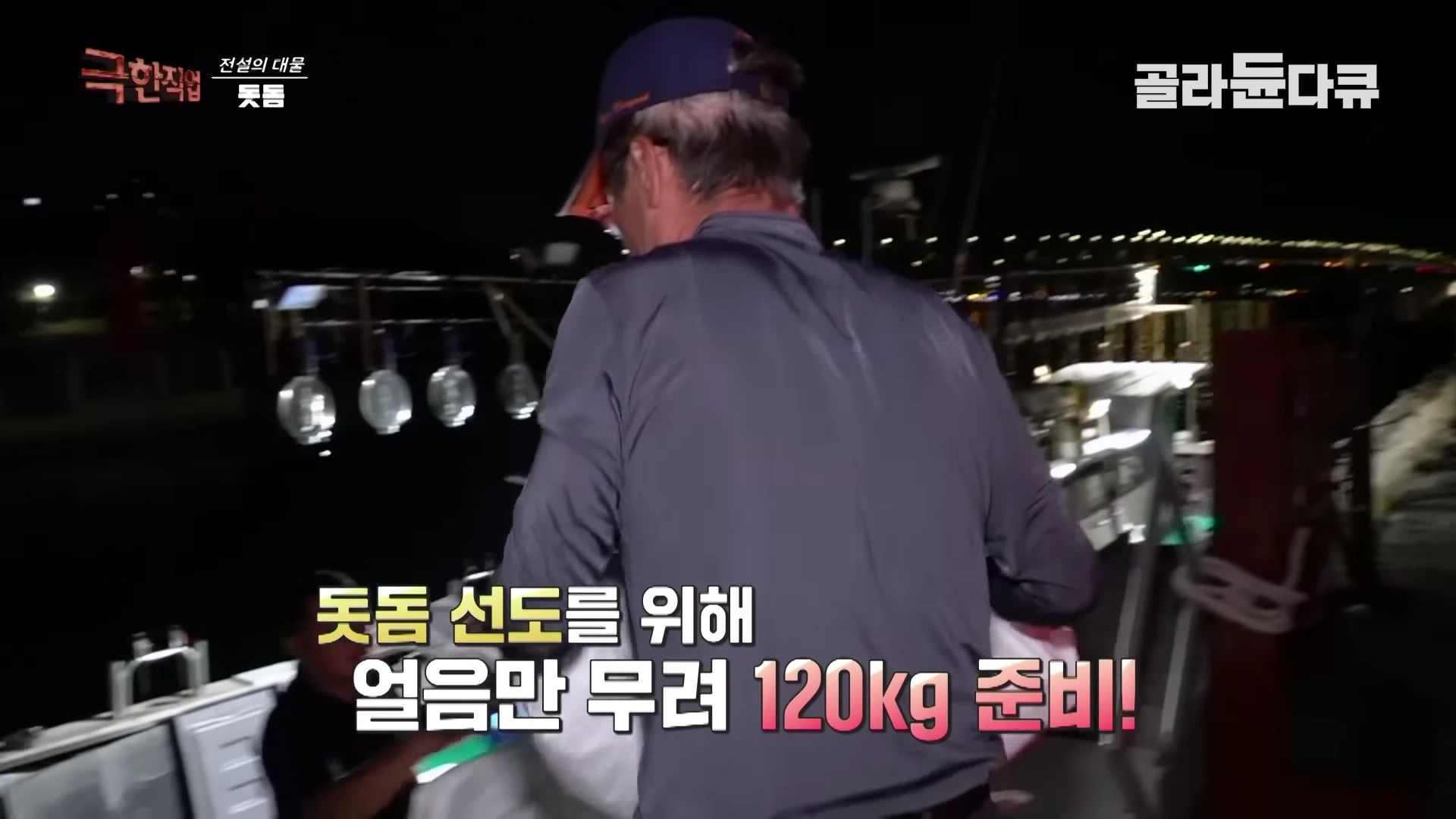 어두운 밤, 모자를 쓴 남성이 배 위에서 짐을 나르고 있으며 화면 중앙에는 '돗돔 선도를 위해 얼음만 무려 120kg 준비!'라는 자막이 표시되어 있습니다.